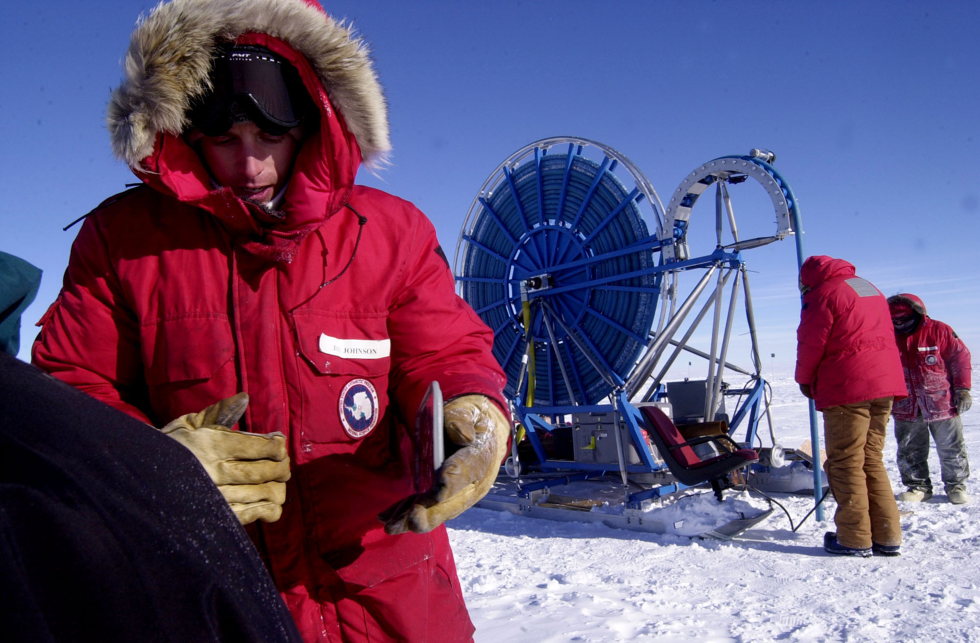 A man talks to someone, while a big round drill rig operates in the background.