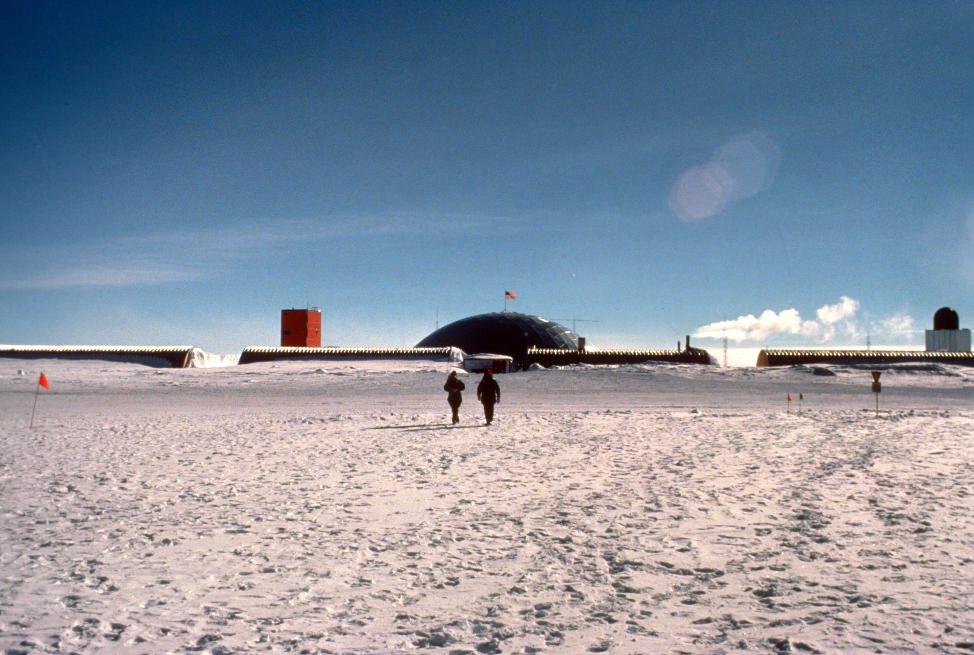 Two people walking towards a dome on a frozen landscape.