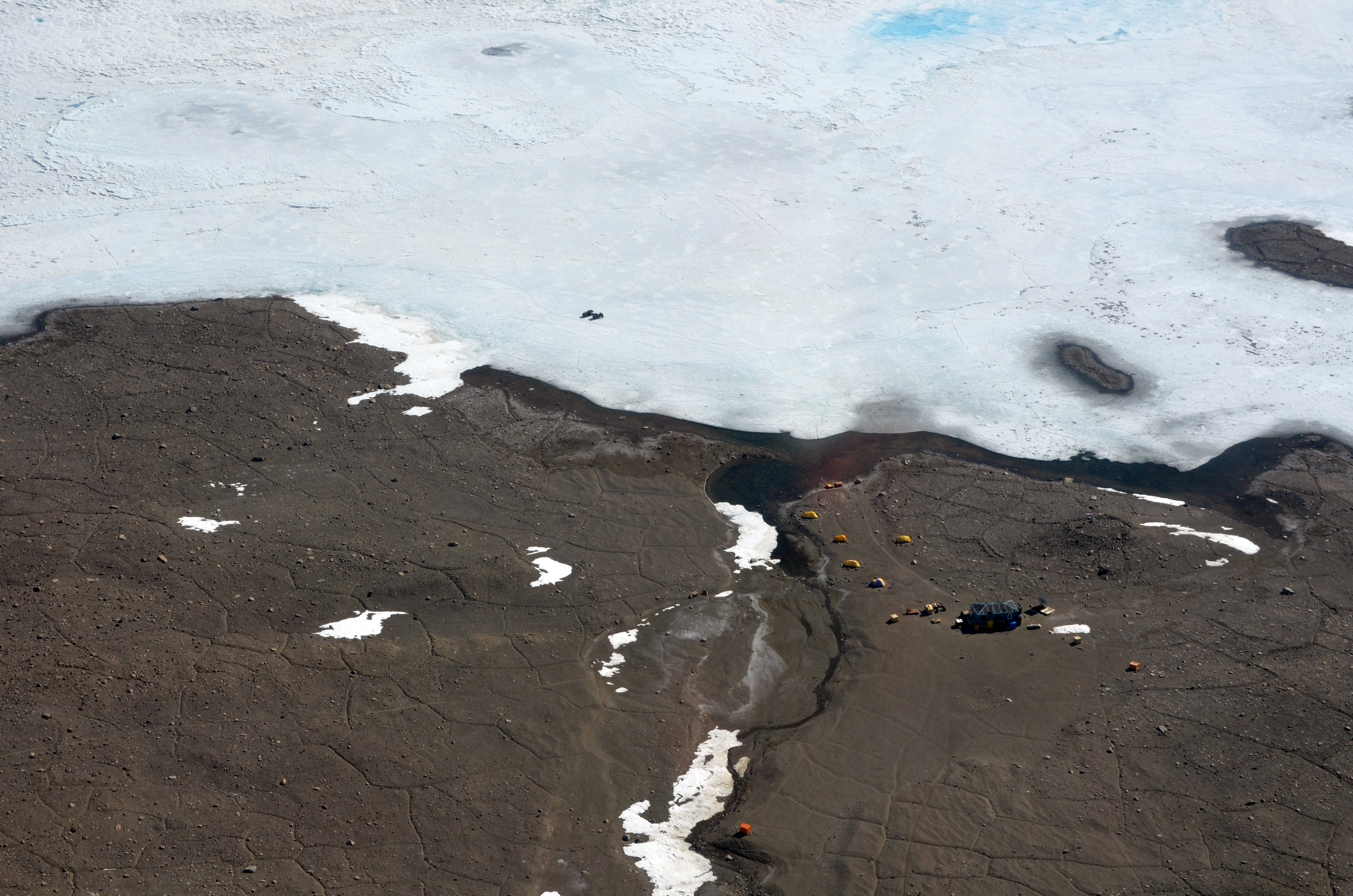 Small buildings near shore of ice-covered lake.