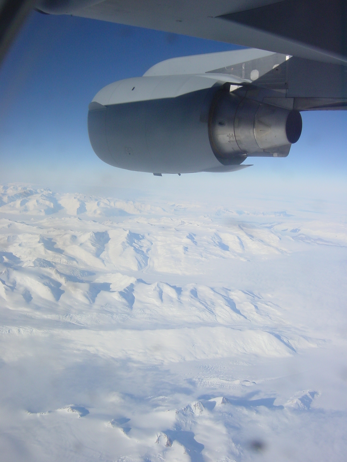 View from jet window of snow covered mountains below.