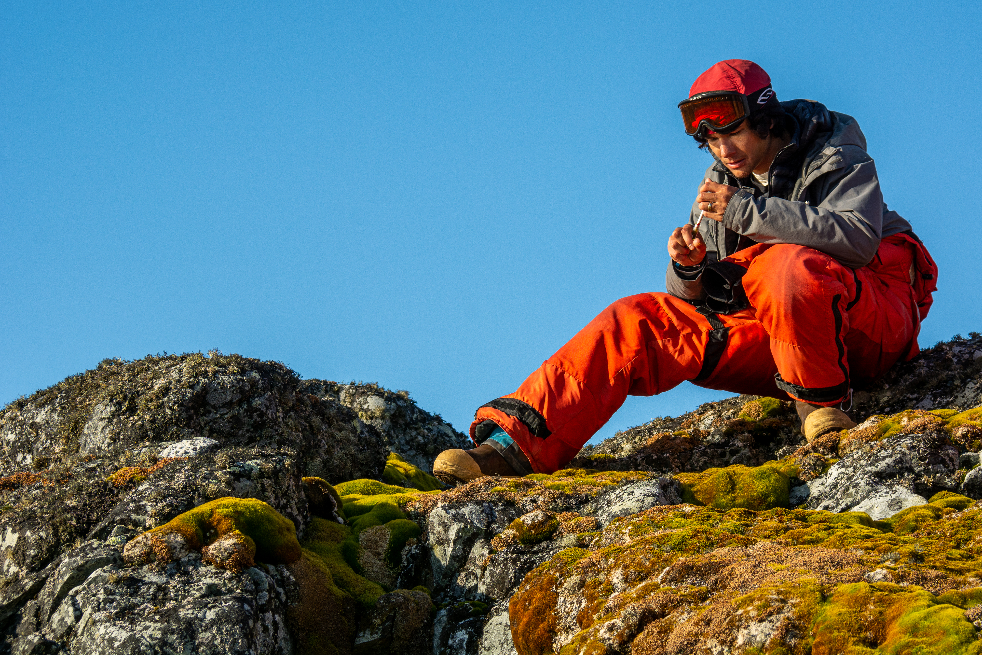 A scientist sitting on a rock picks up pieces of moss