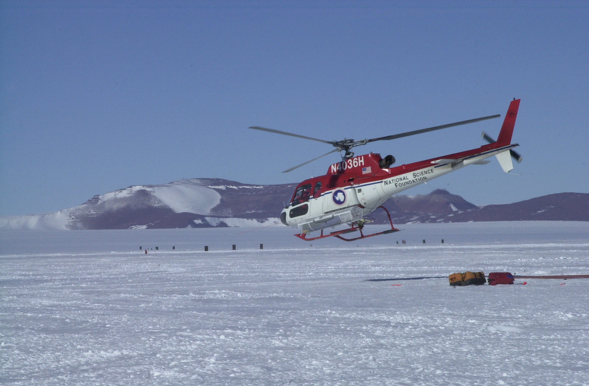 A helicopter lifts off from a snow-covered surface.