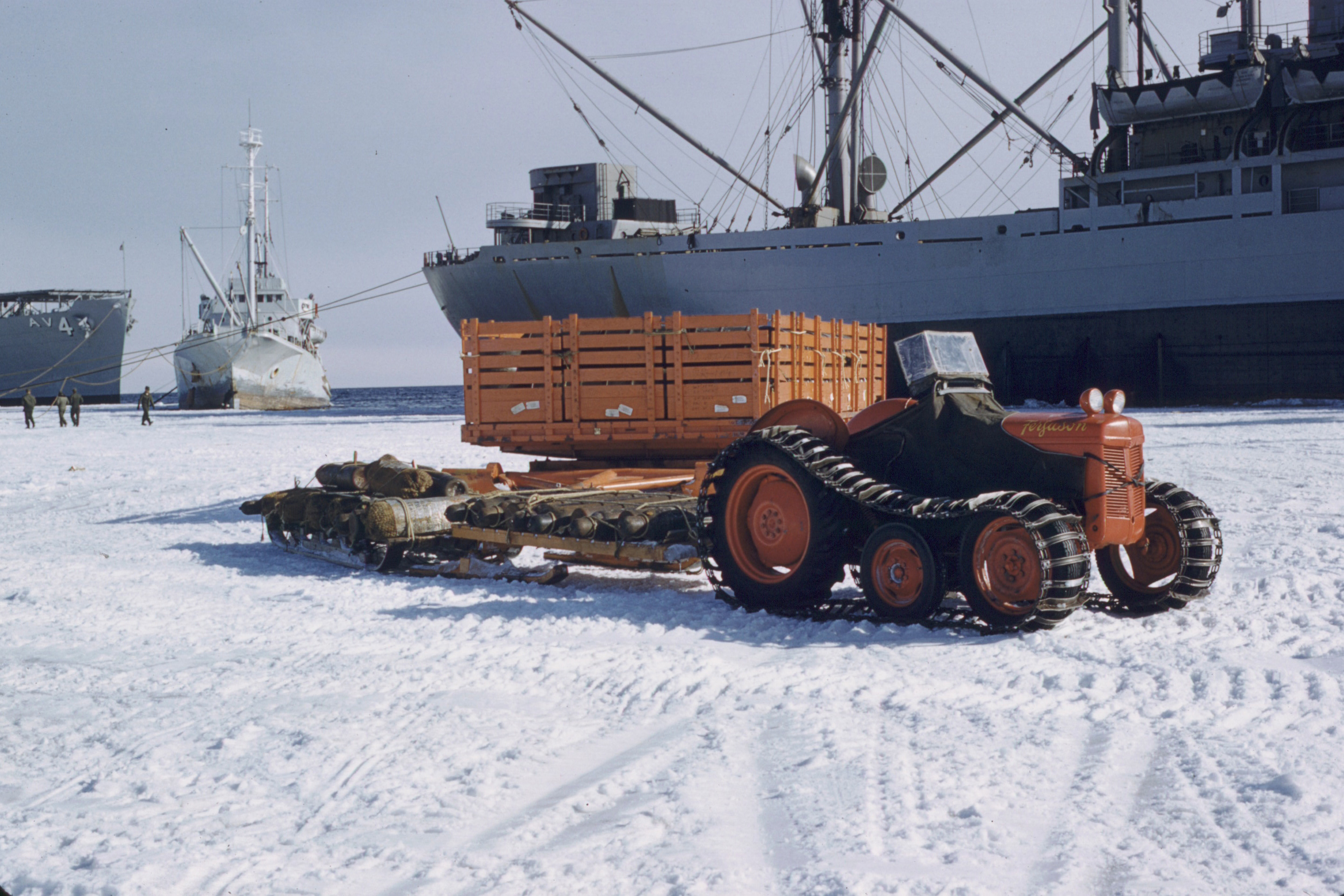 A small orange tractor sits on ice near several ships.