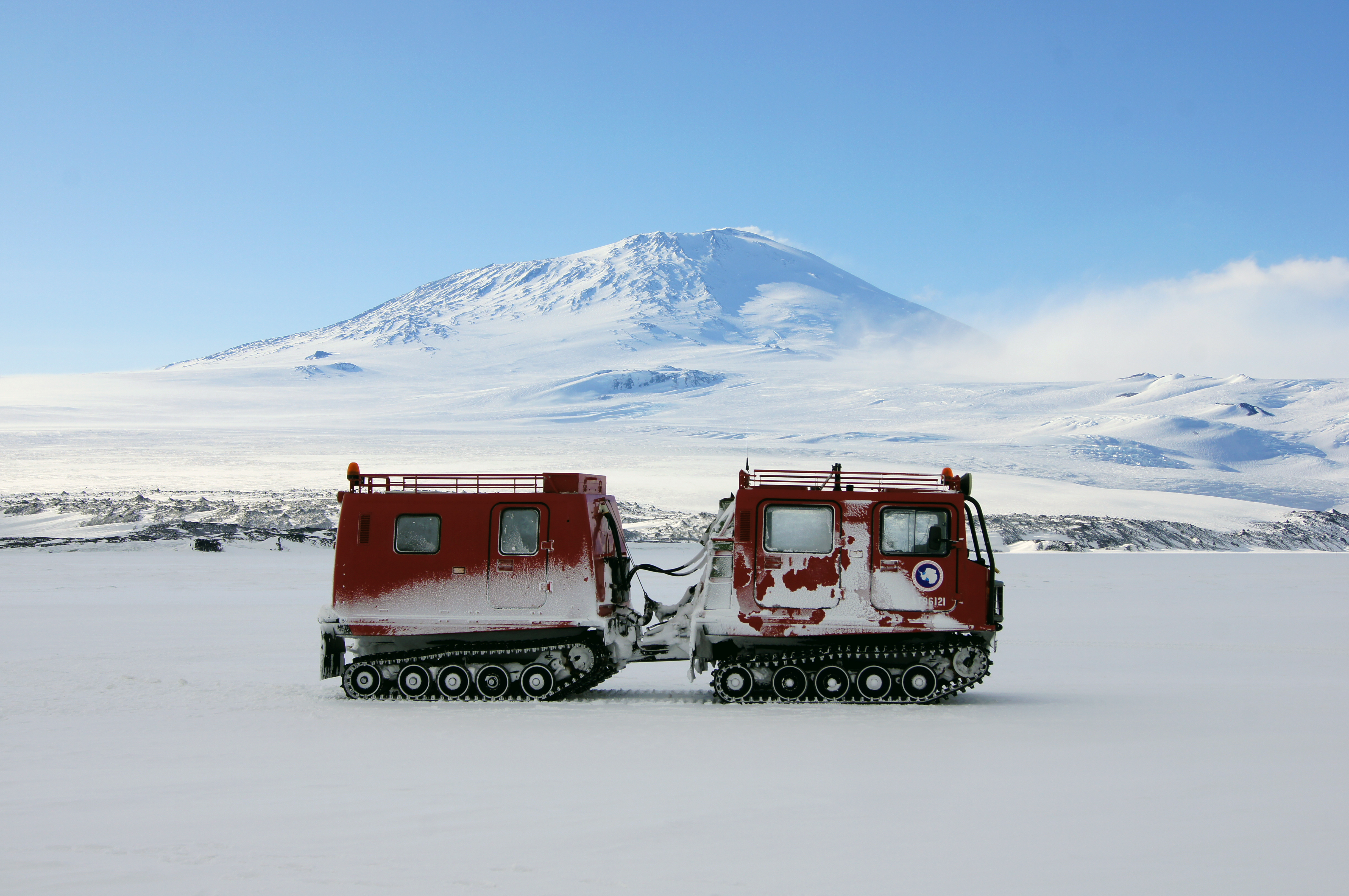 A tracked vehicle on ice sits in front of a mountain.