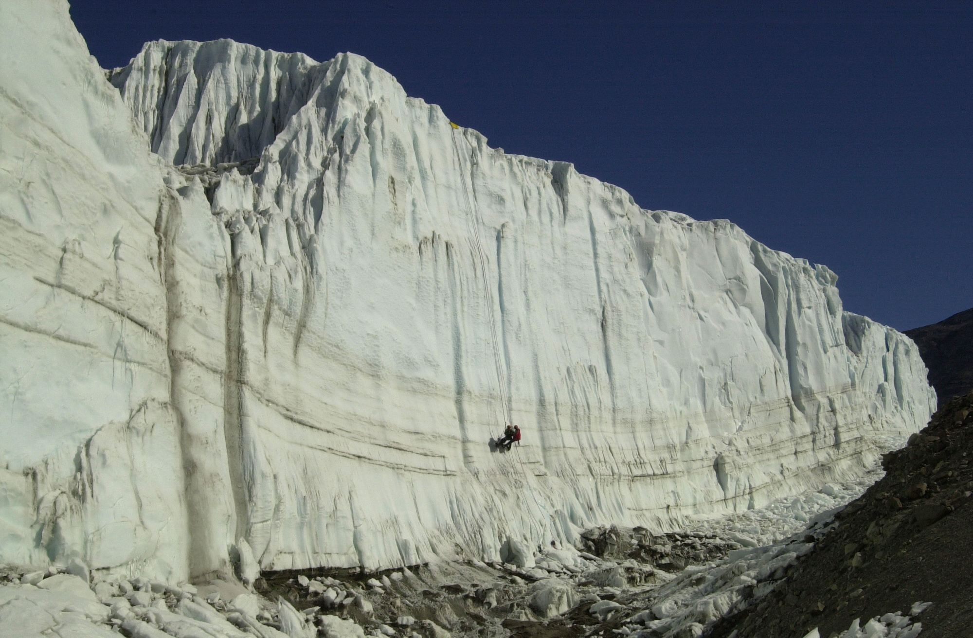 Two people climb up an enormous ice cliff.