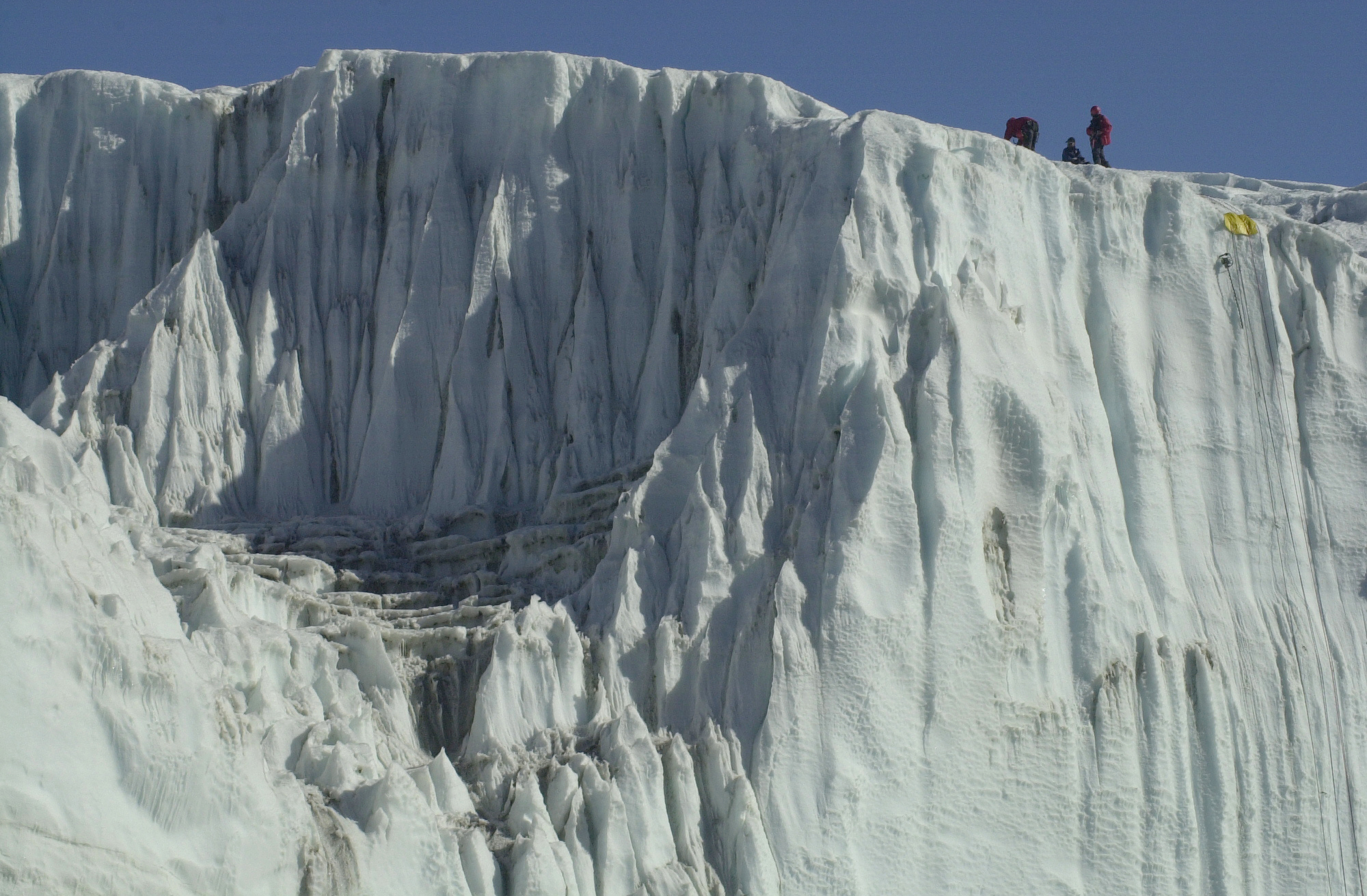 Three people at the top of an ice cliff. 