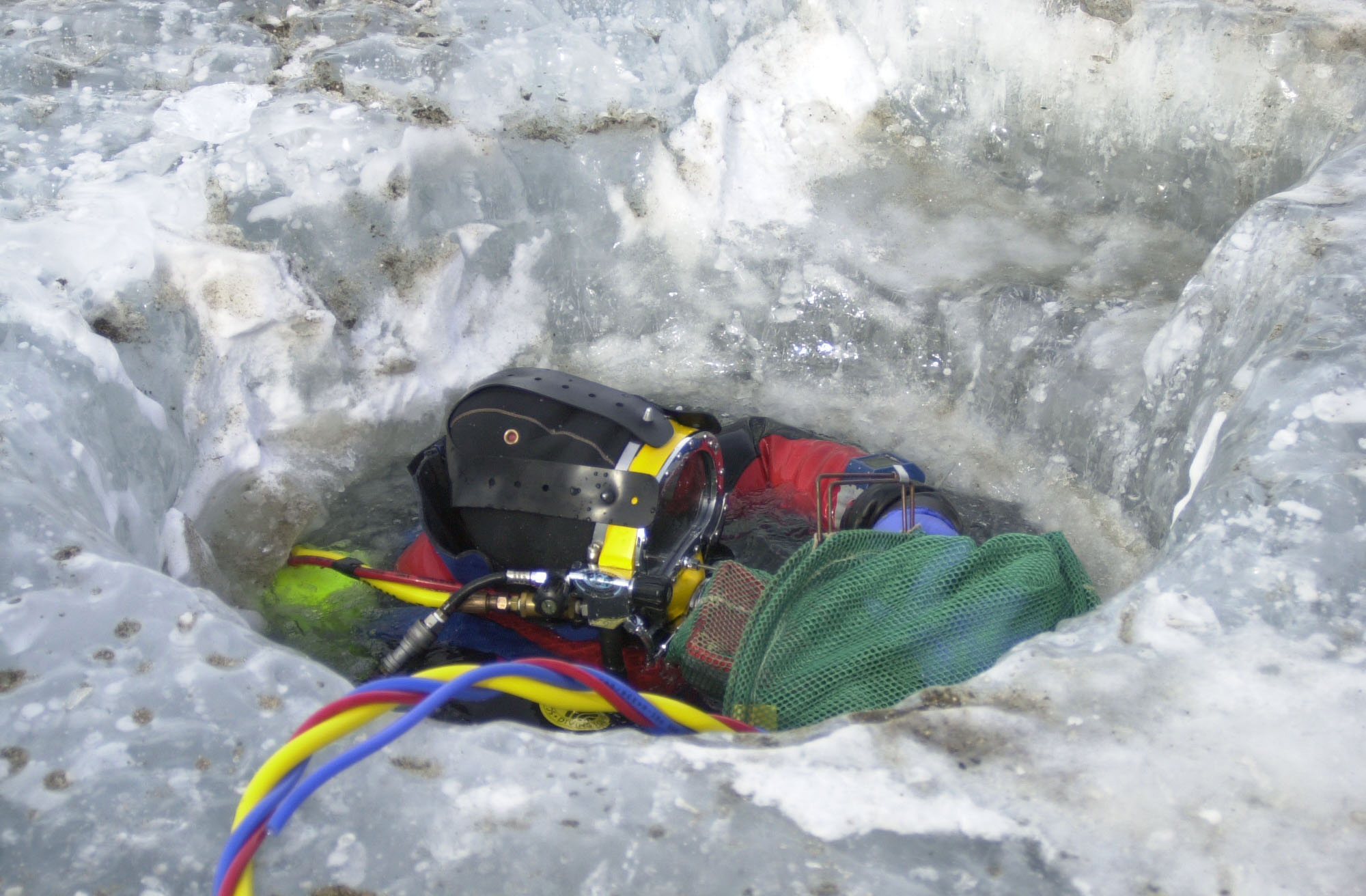 A SCUBA diver's head can be seen in a hole in the ice.