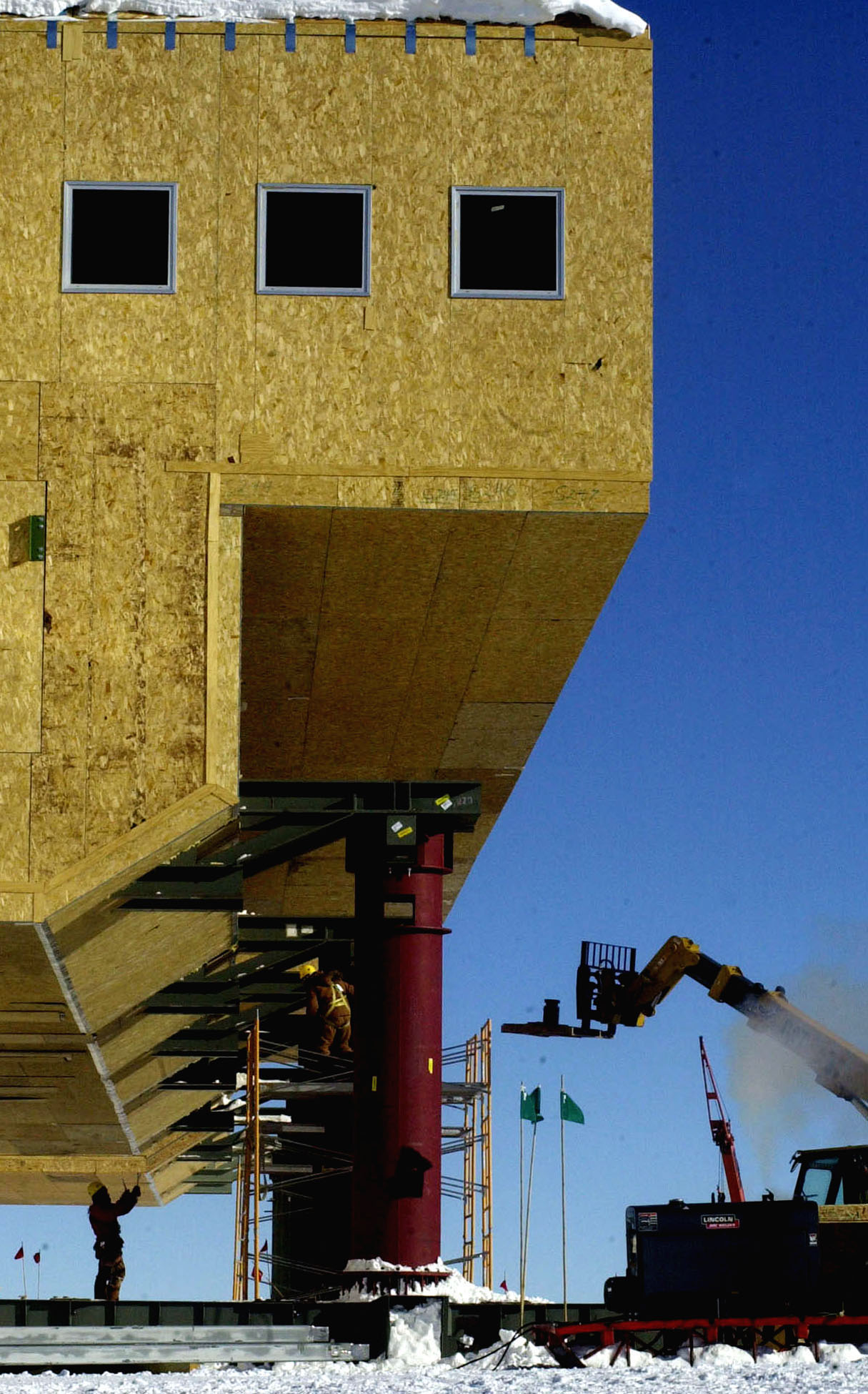 A man, left, and a crane, right, guide other workers near the columns of a building.  