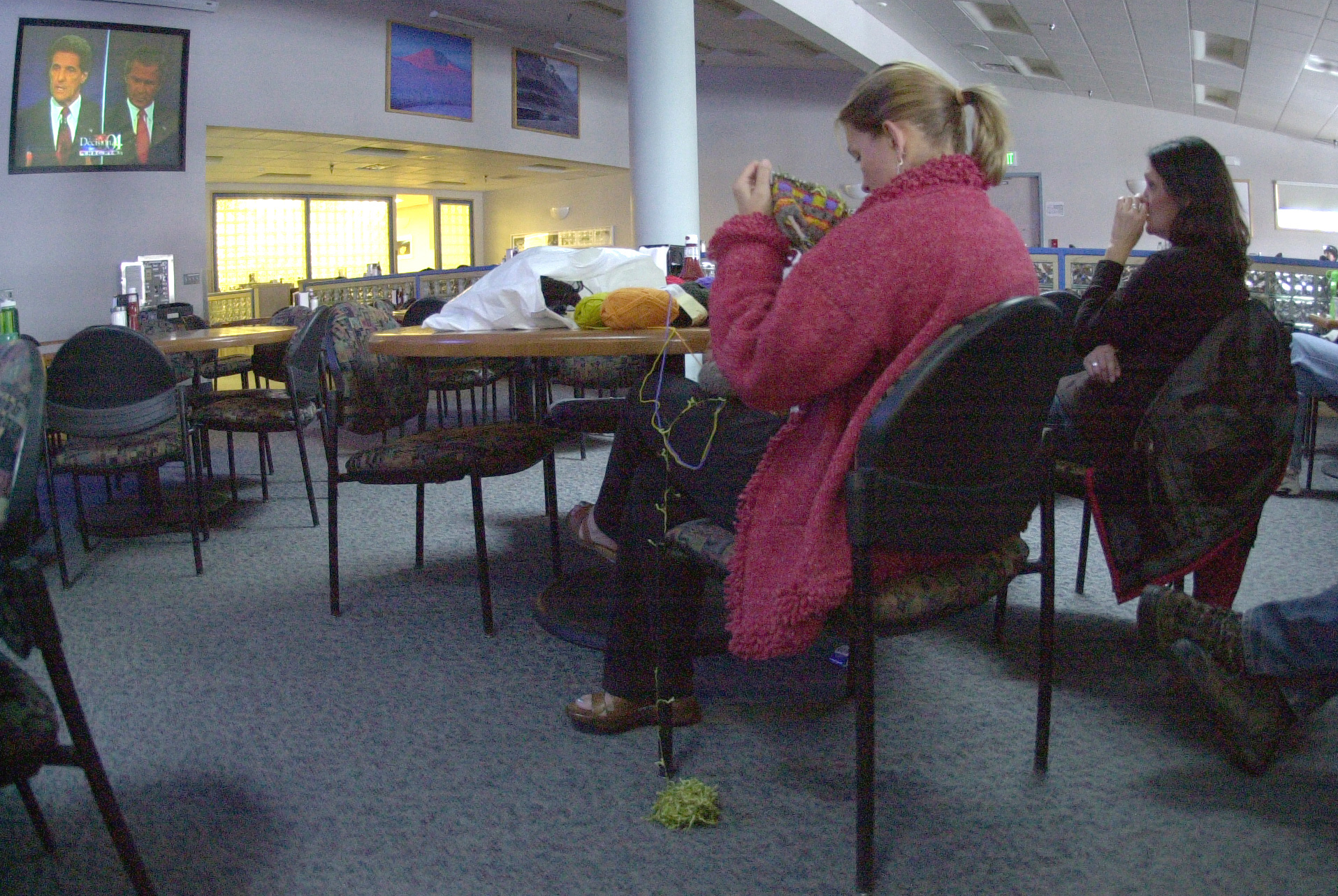 Two women sit in chairs with a TV on in front of them.