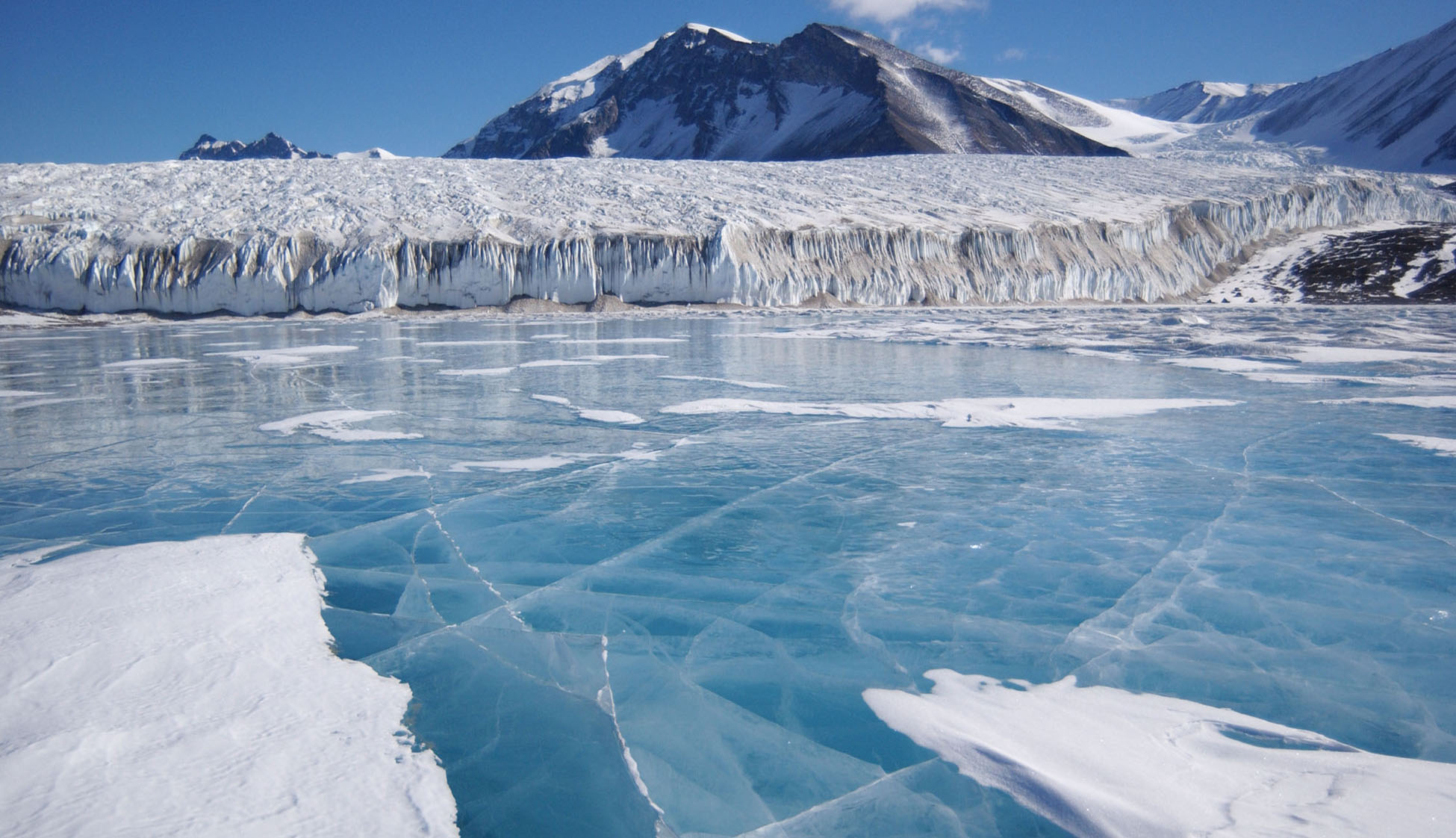 A frozen lake next to a glacier.  The ice is turquoise blue.