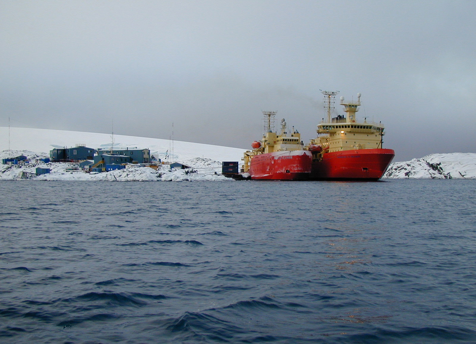 Two ships moored by a cluster of buildings.