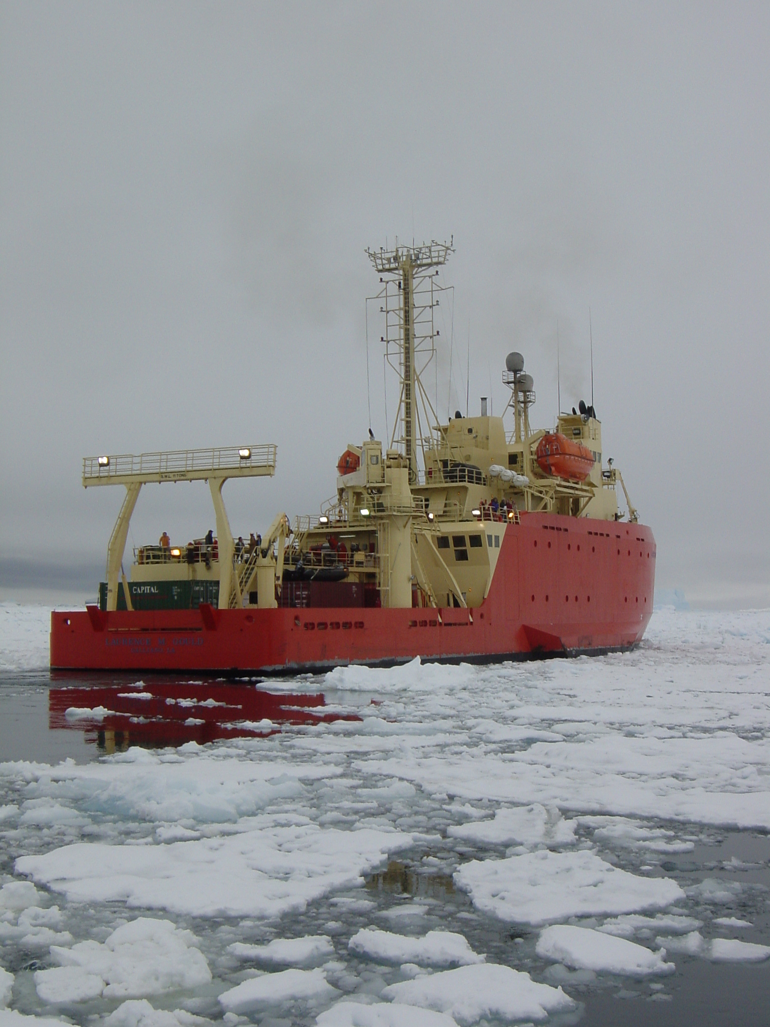 The starboard side of a red and yellow ship in icy water.