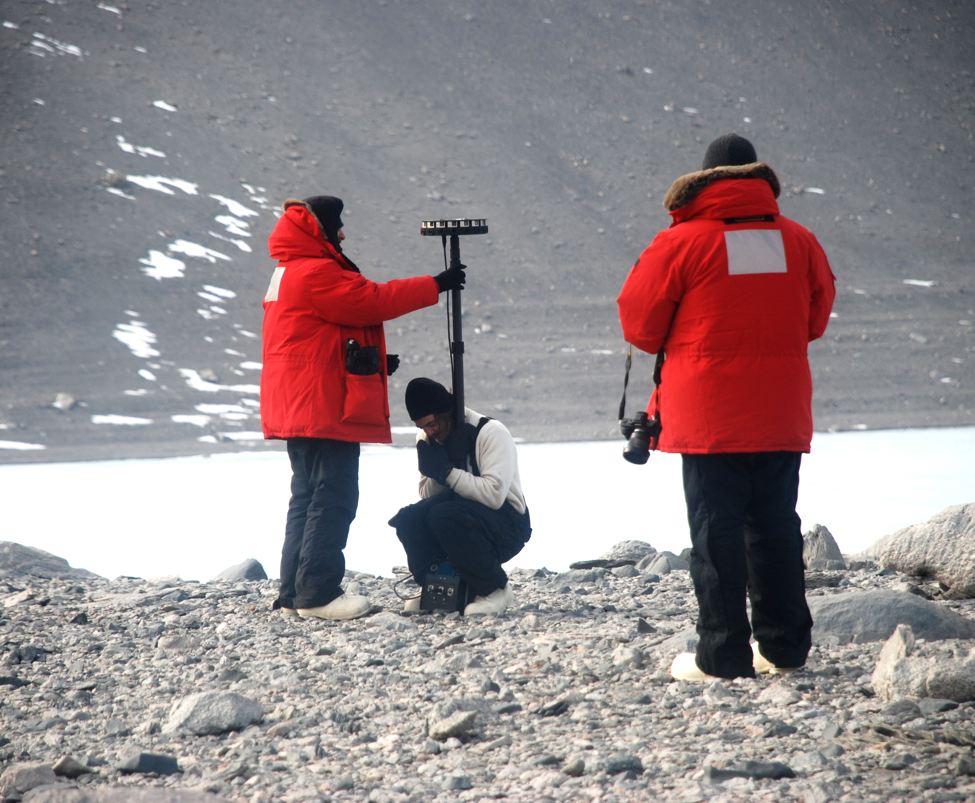 People position a camera in a rocky terrain.