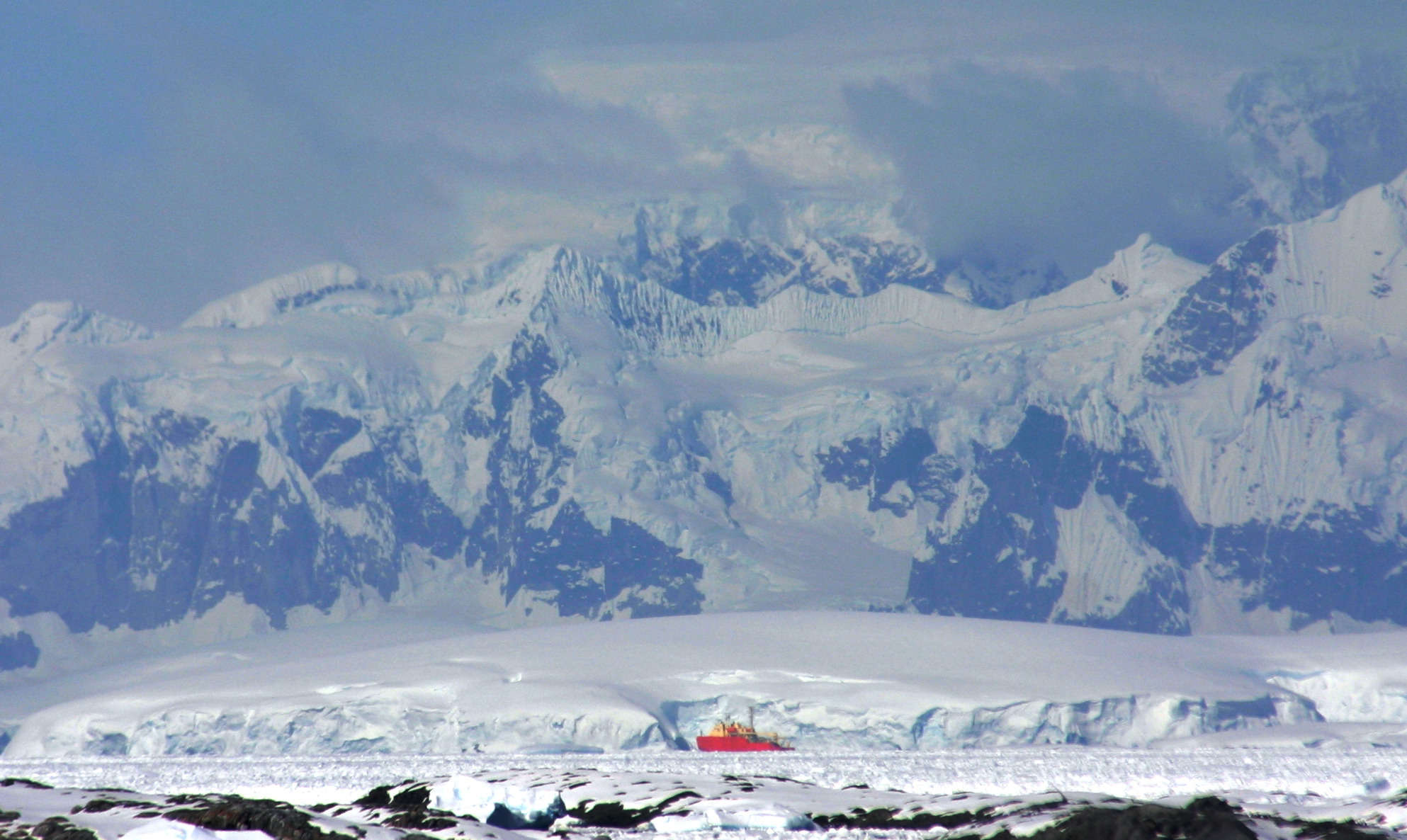 A red ship appears in the distance with mountains behind it.