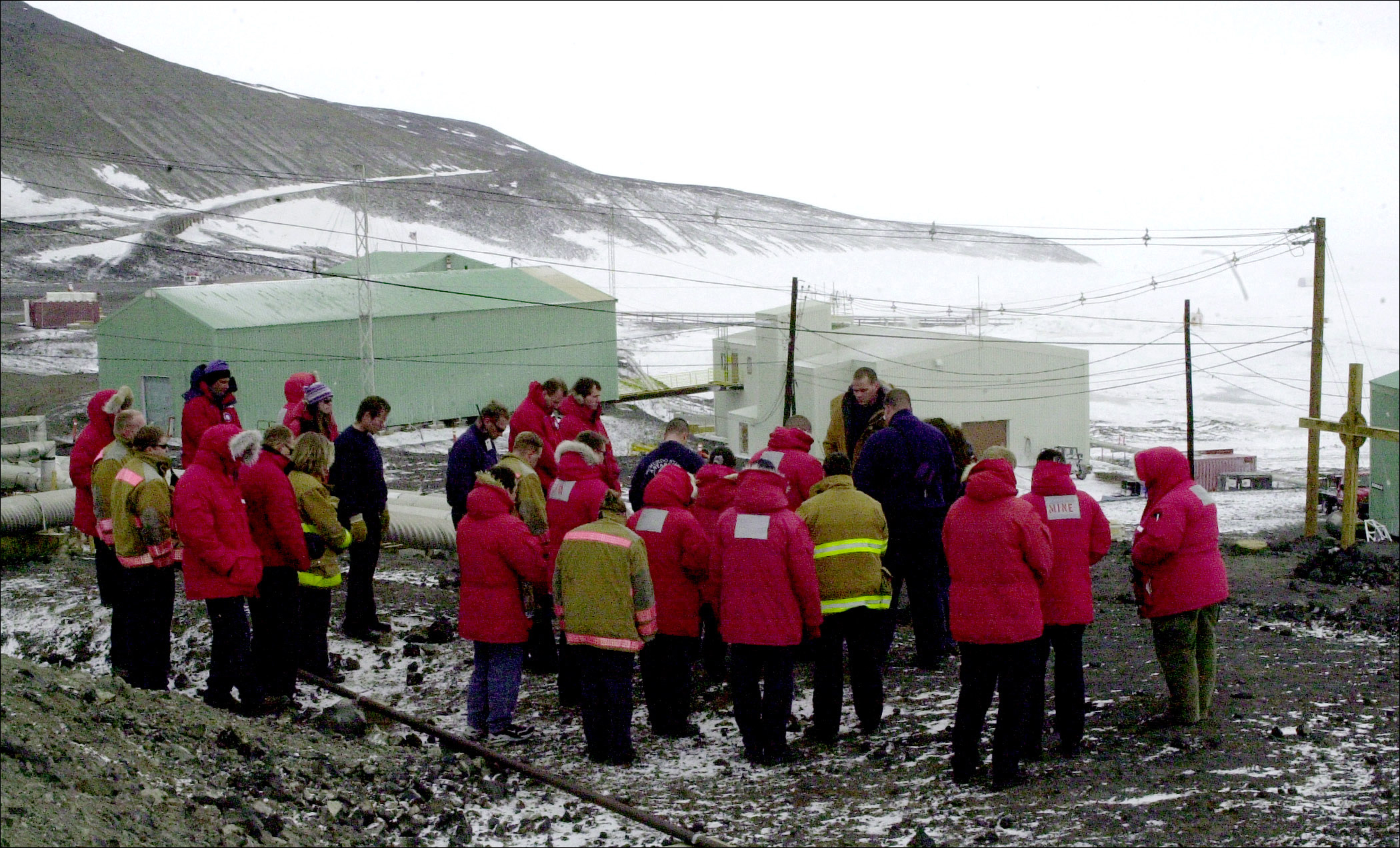 Group of people dressed in heavy parkas bow their heads.