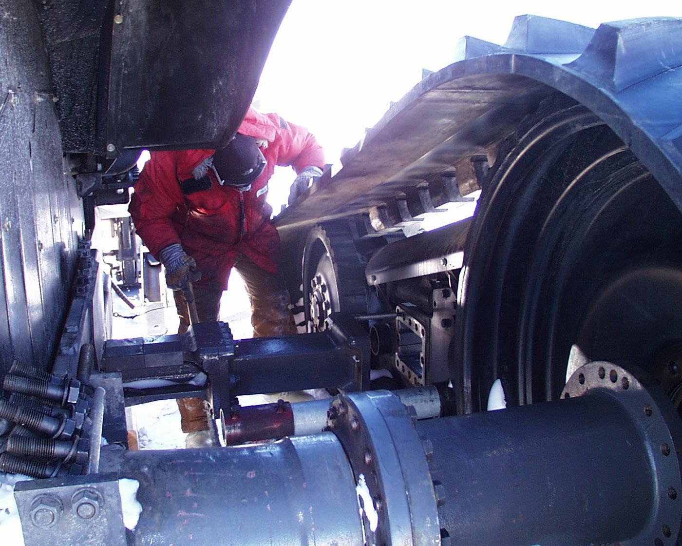 A man in a red parka bends over a large track on a tractor.