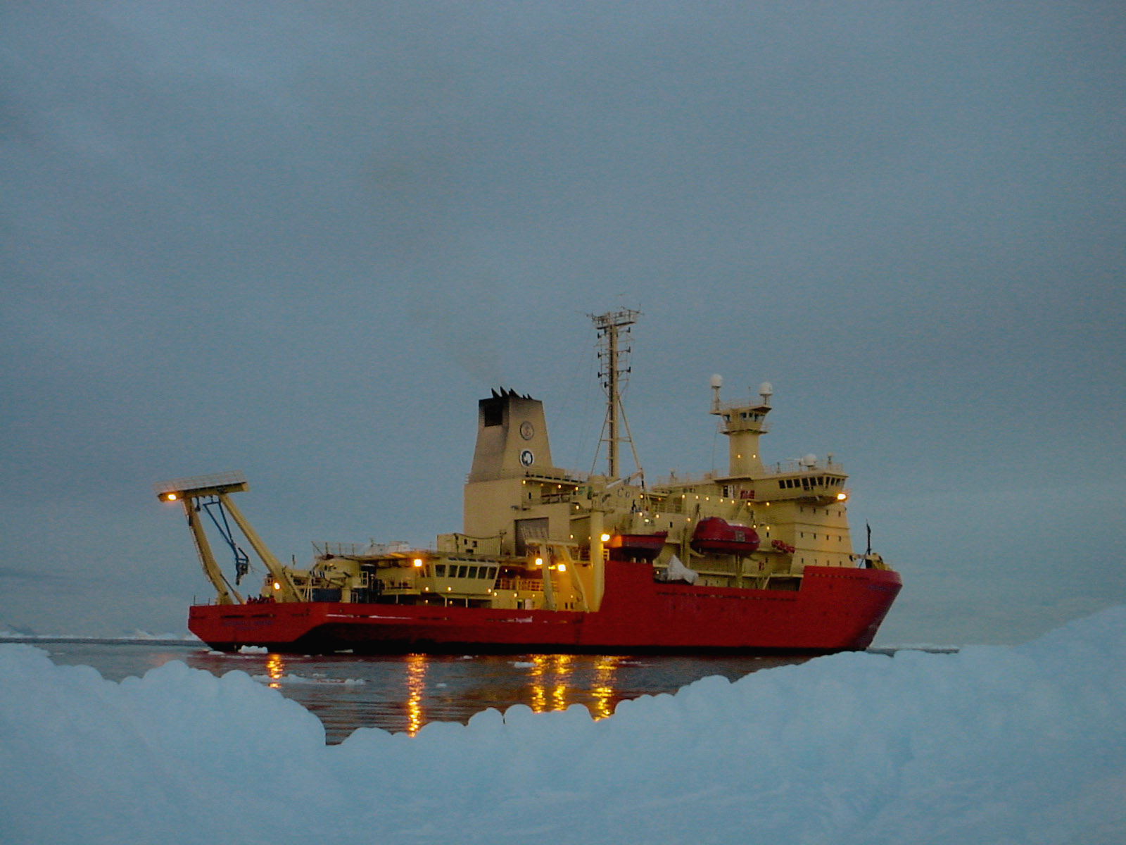 A ship sits in the water near a snow covered embankment.