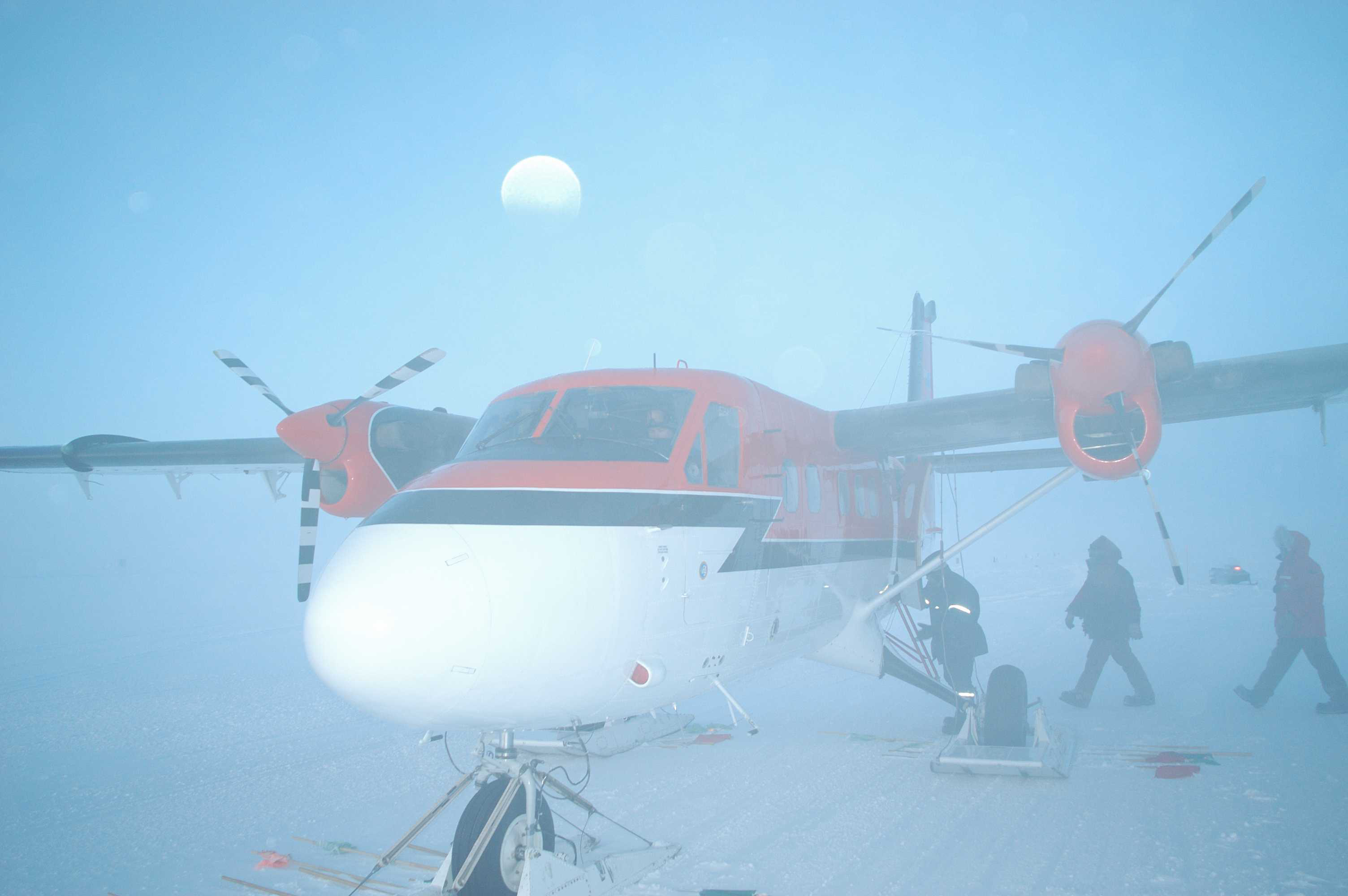 People gather near a small airplane, while the moon can be seen in the background.