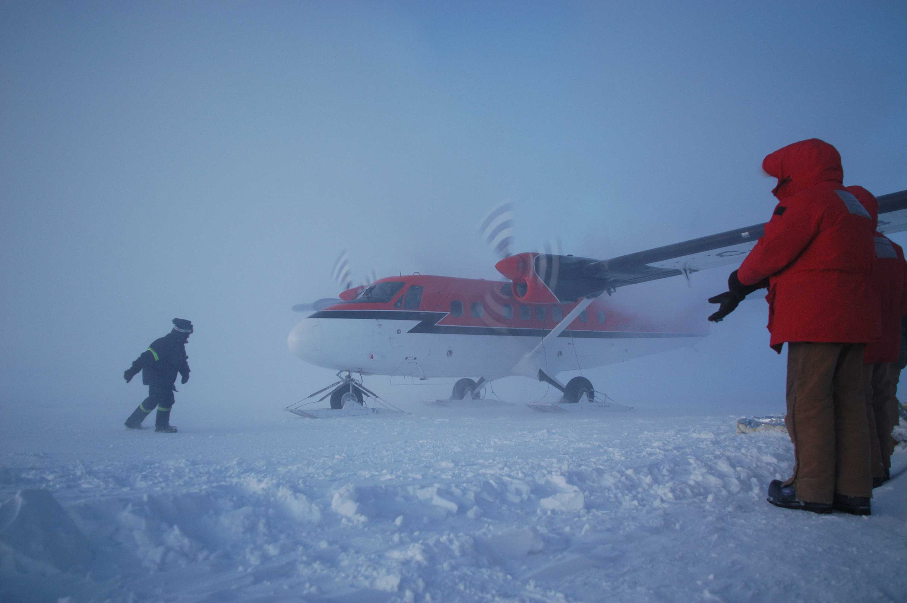 People stand close to a twin engine airplane on skis.