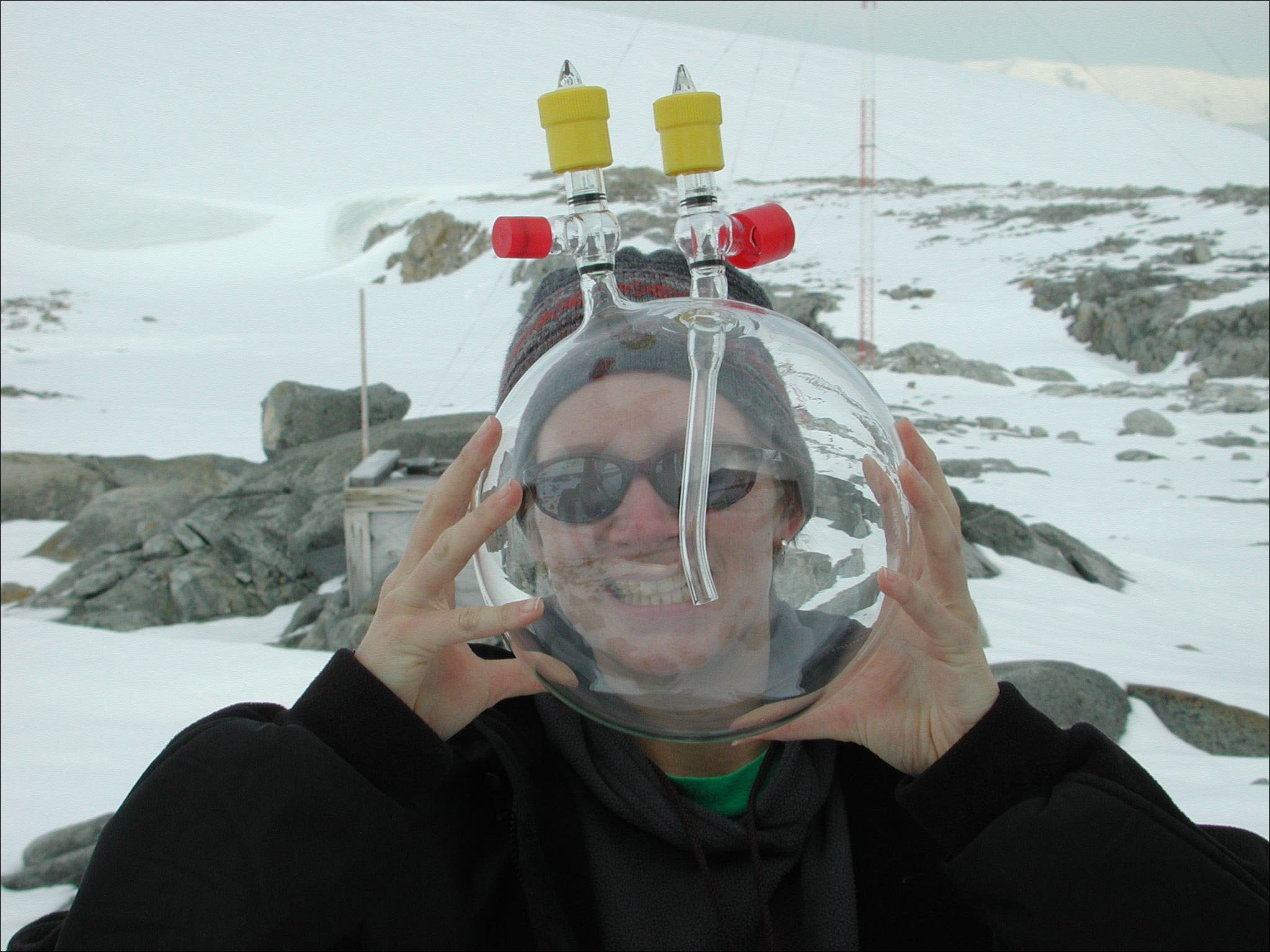 A woman peers through a cylindrical glass flask.