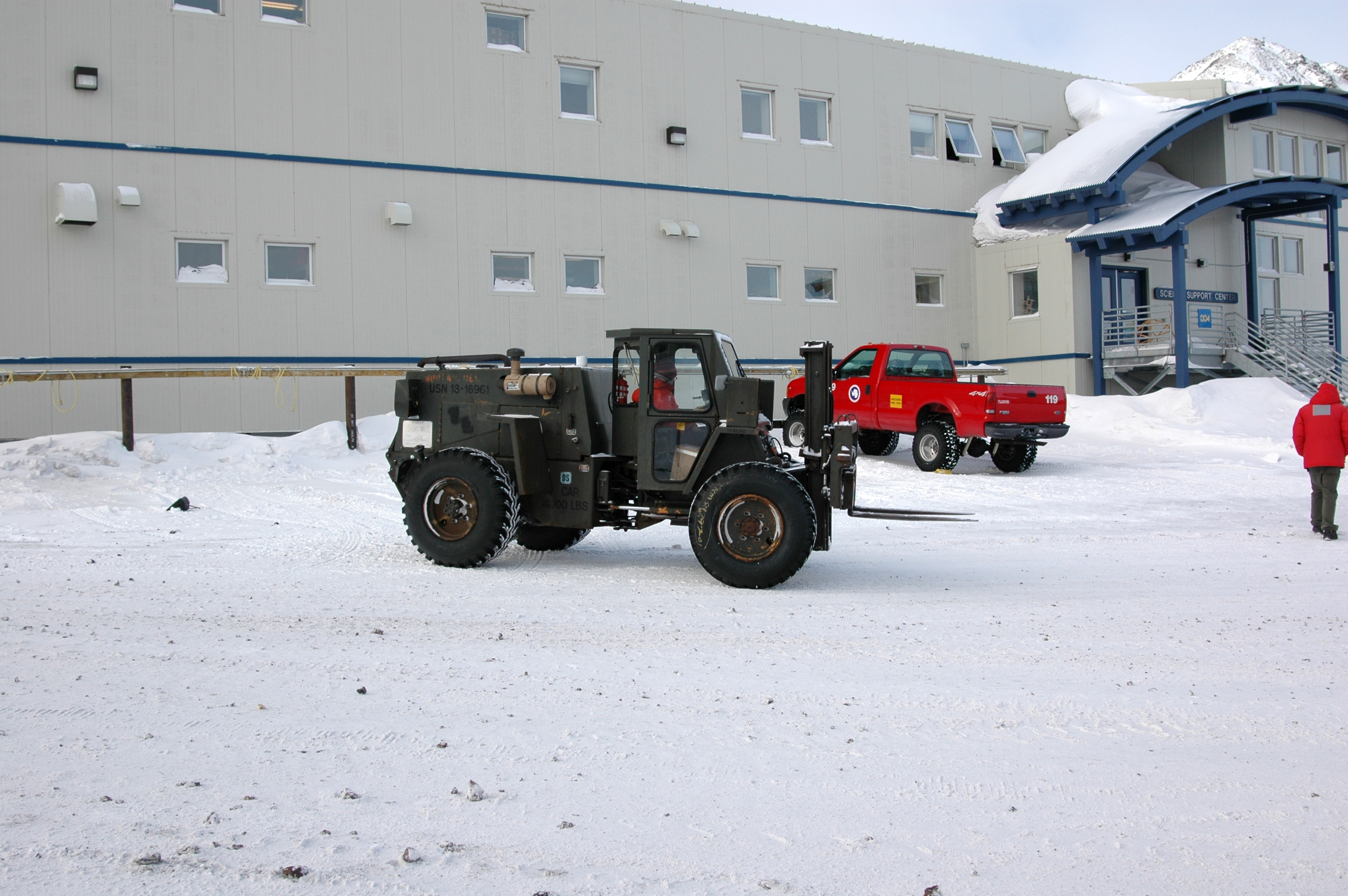 A small forklift drives on snow.