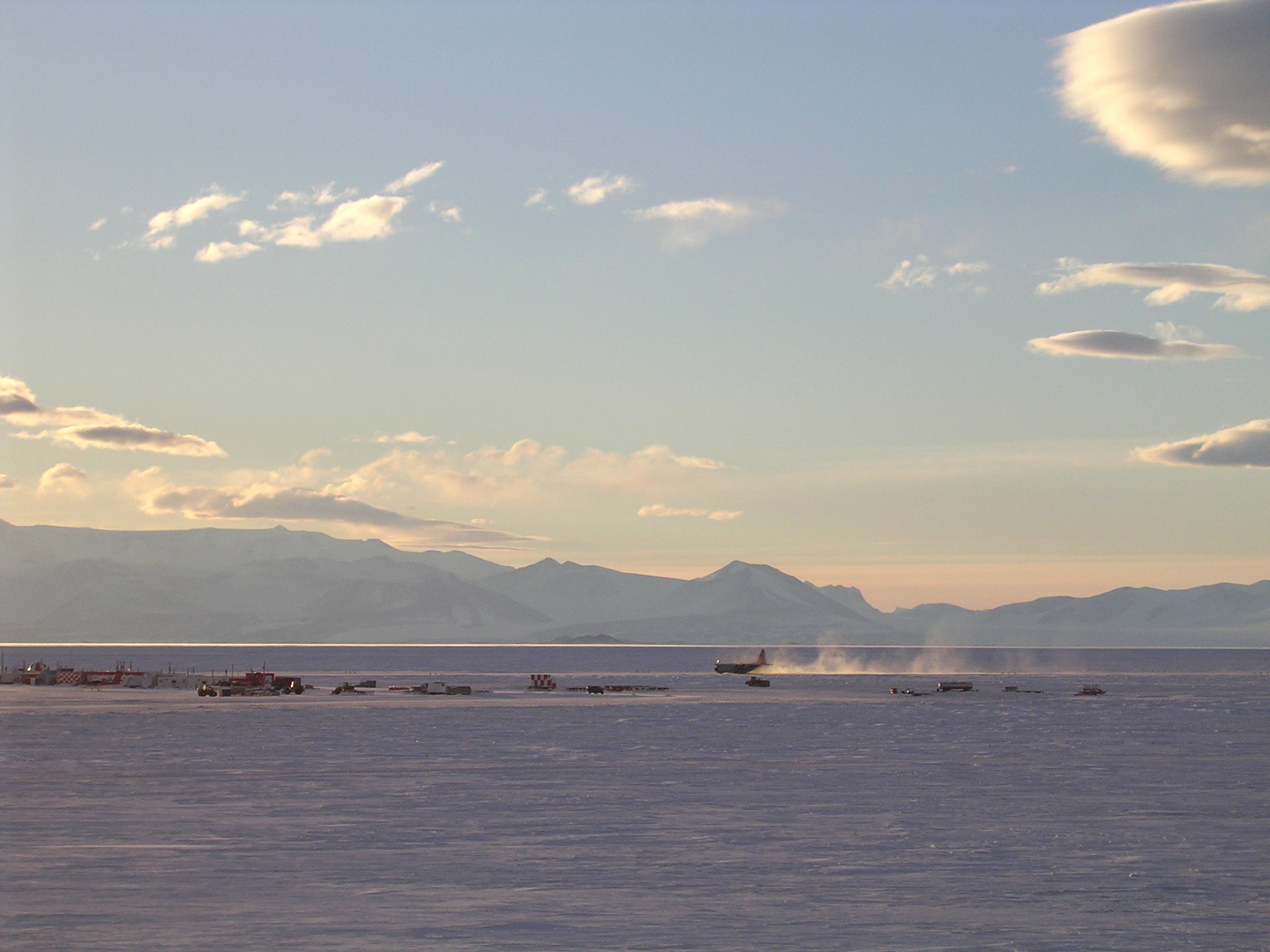 Plane landing on snow with mountains in background.