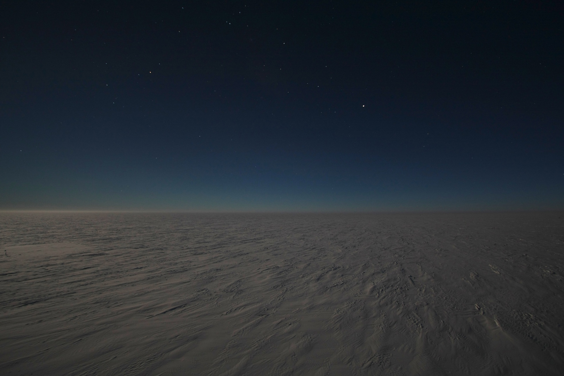 Flat white snowy landscape at night.