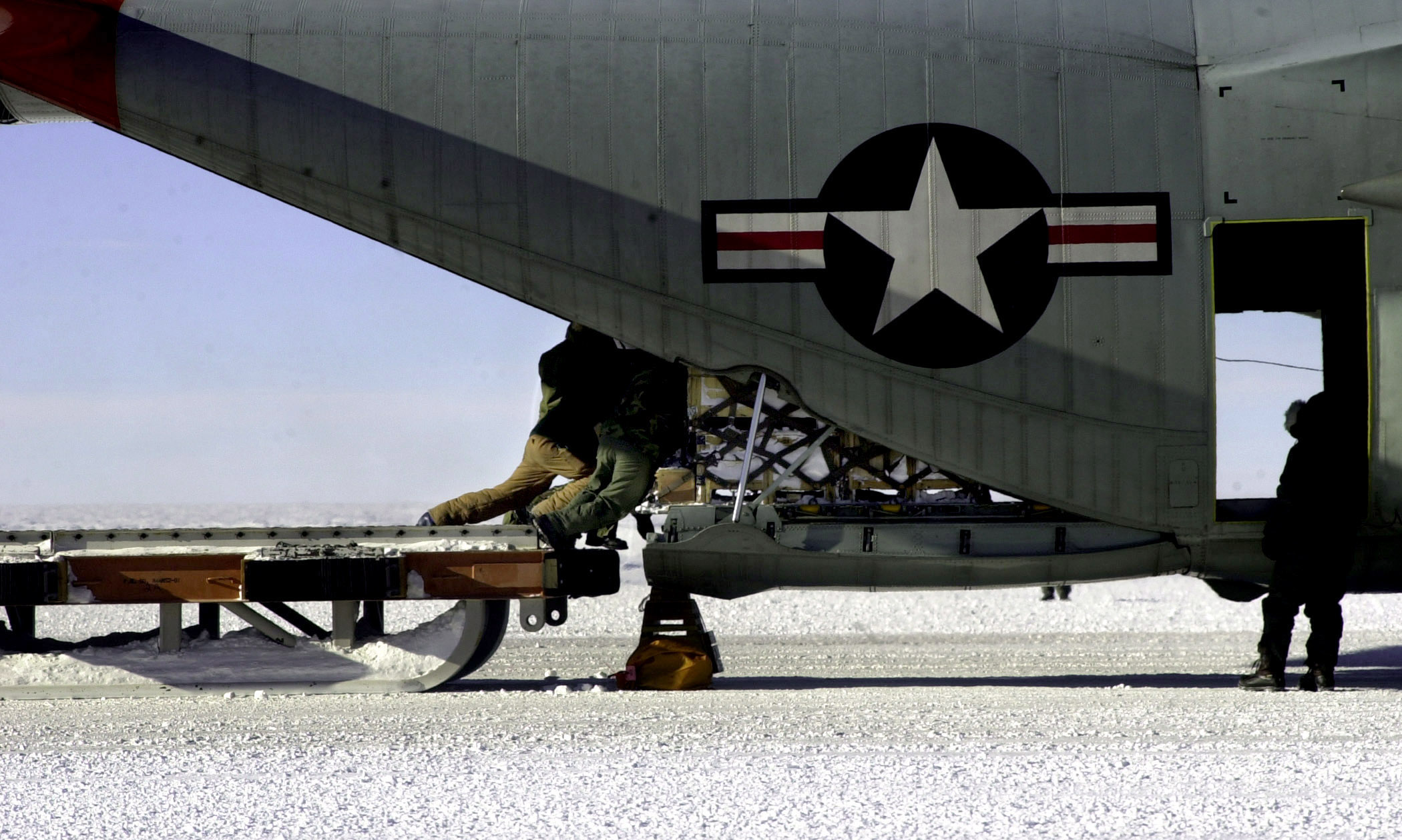 Three people push a pallet of cargo into the rear of an airplane.