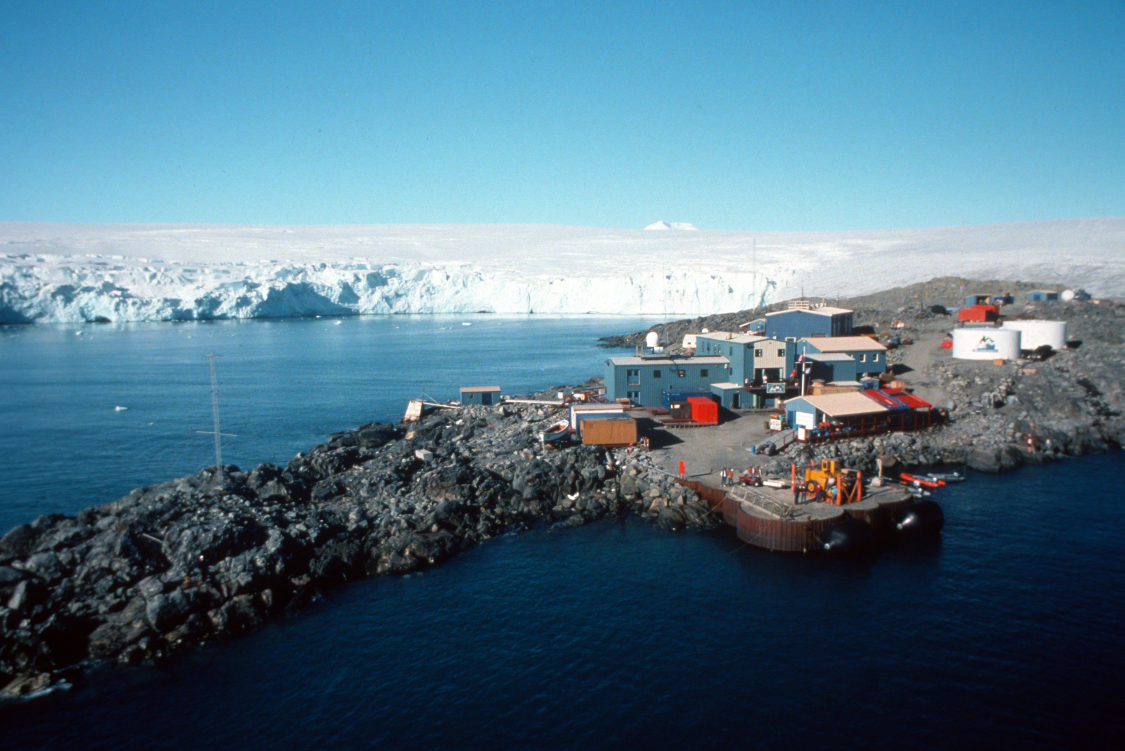 Buildings on a rocky coastline with frozen landscape in the background.