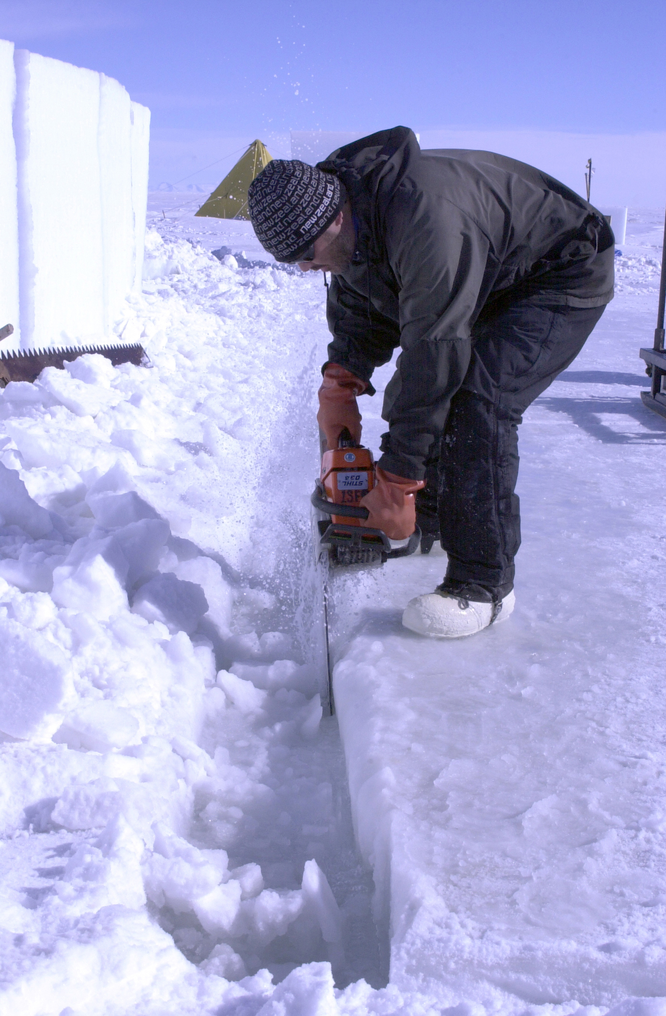 A man uses a chainsaw to cut ice. 