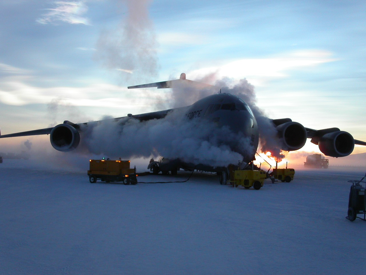 A jet on ice, with small vehicles near it.