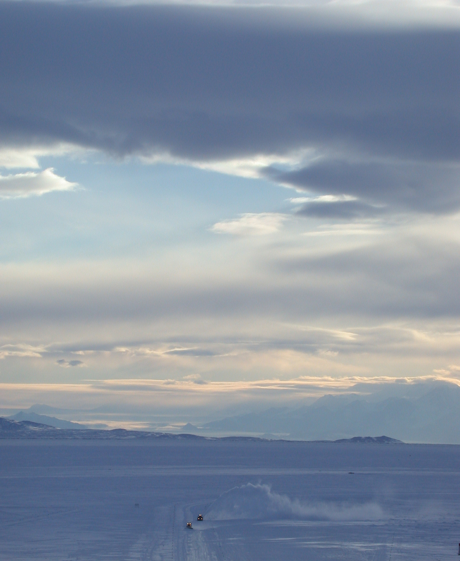 A snowplow on ice with mountains in the background.