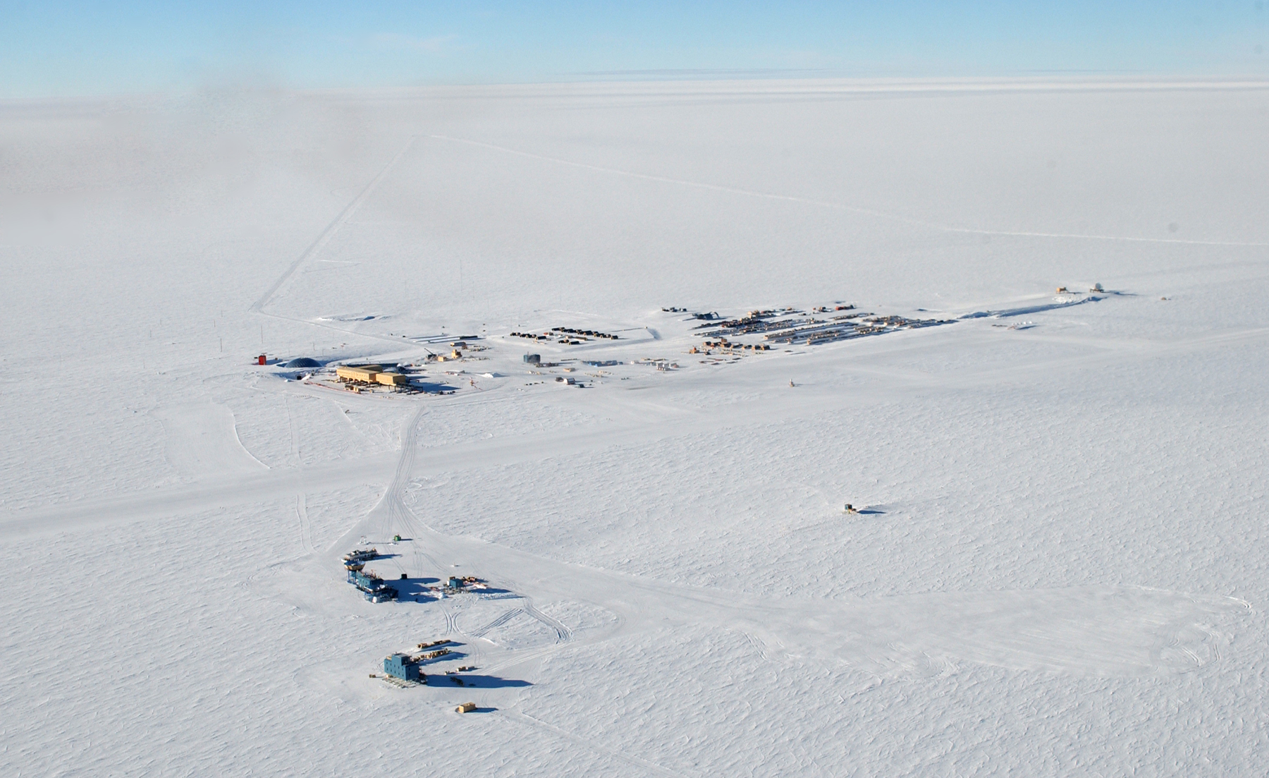 Aerial view of a small cluster of buildings on a snow-covered plateau.