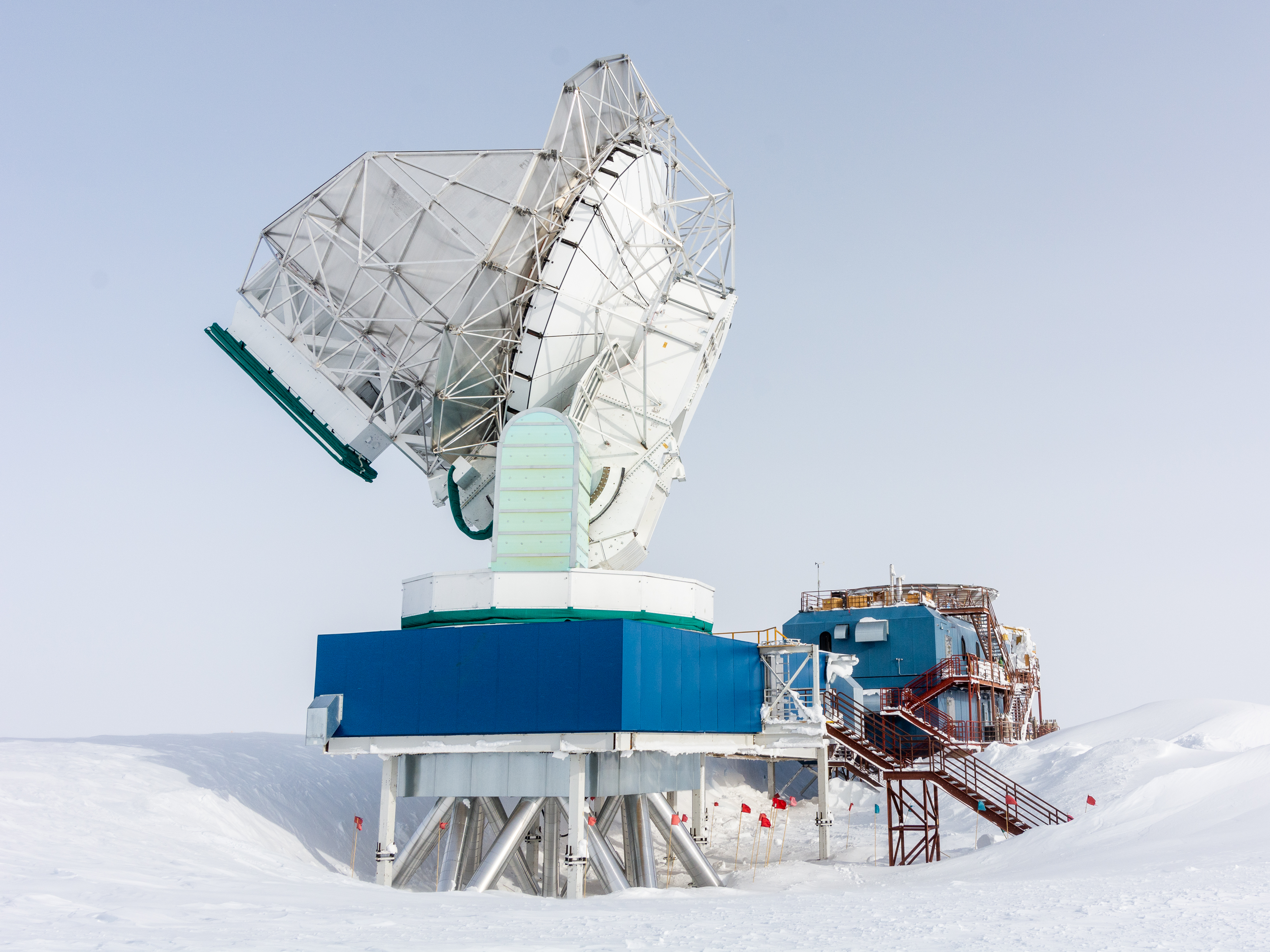 A radio telescope pointed at the sky with a snowy landscape around it.