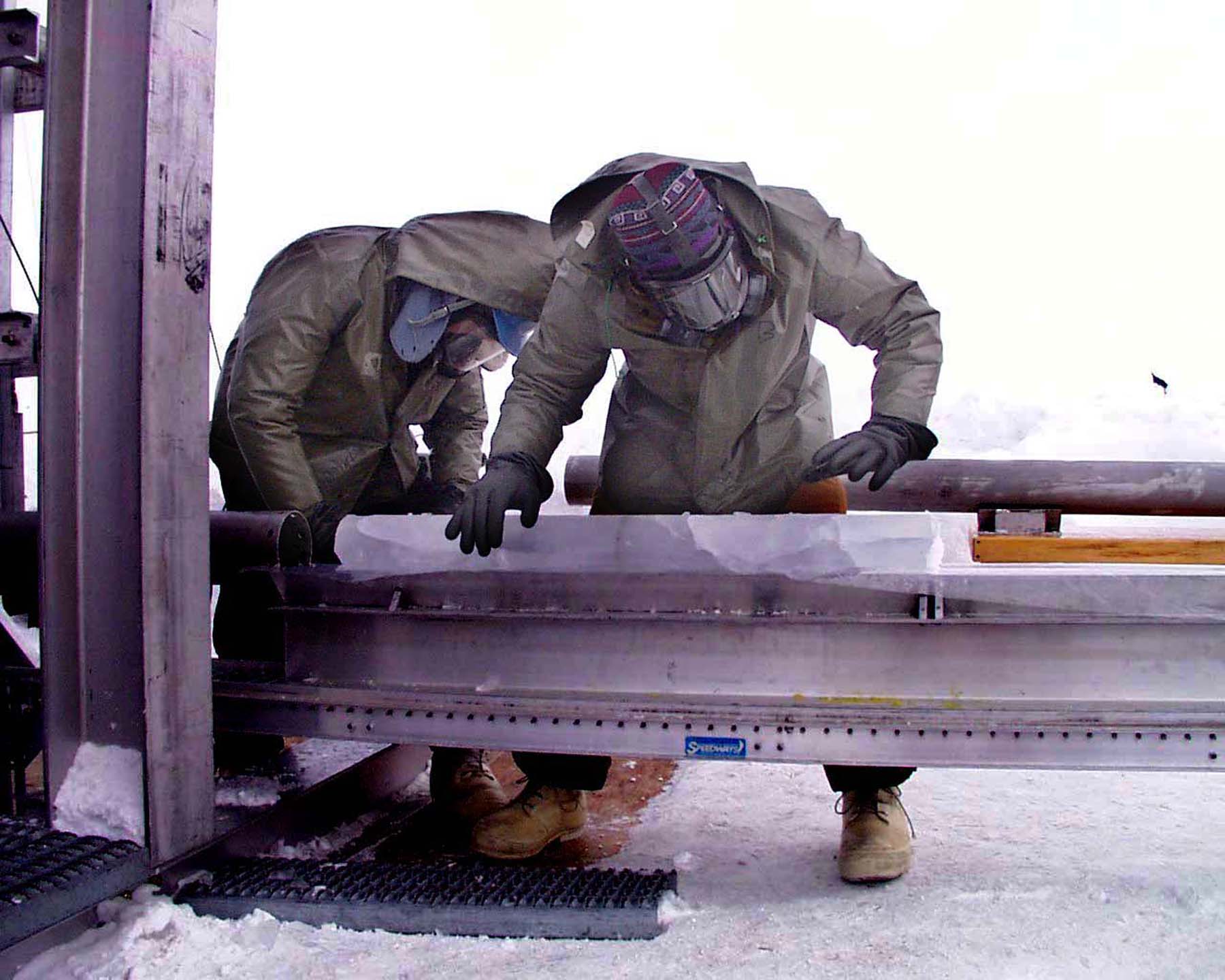 Two men lean over an ice core on a machine.  