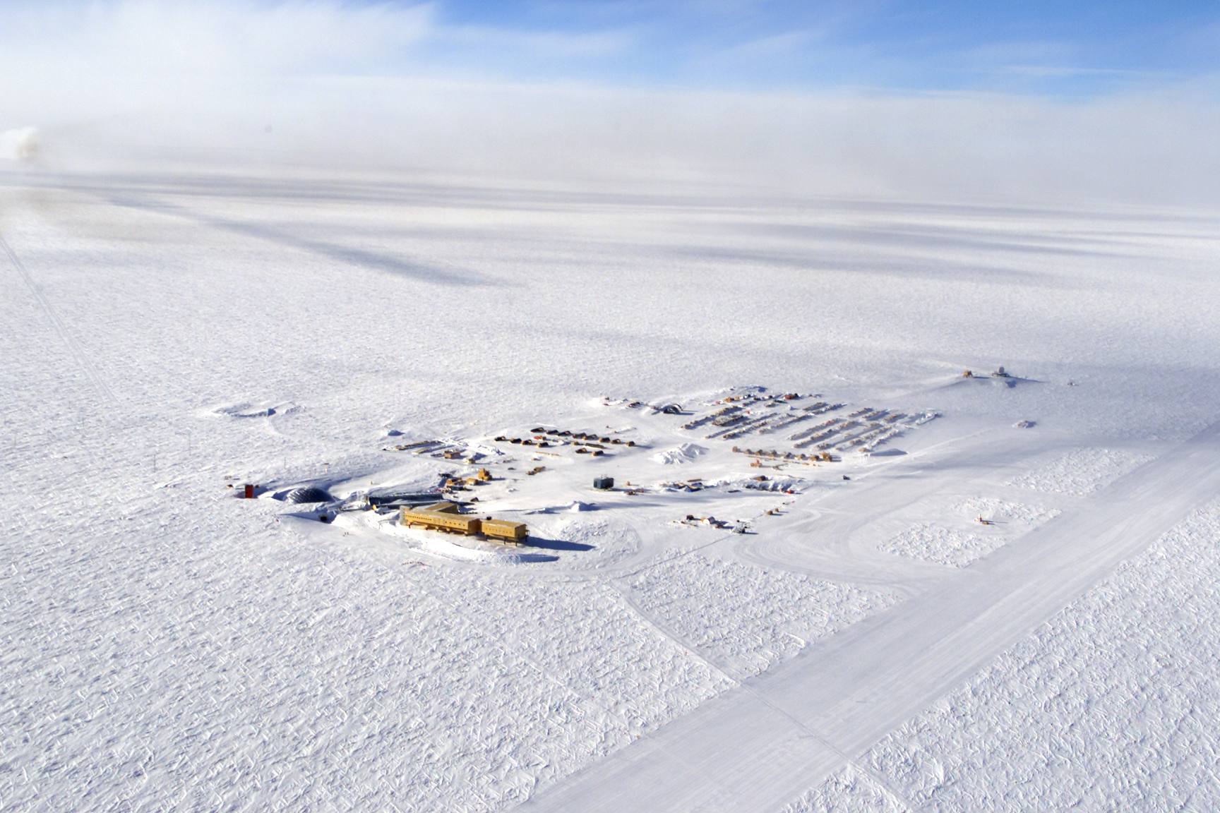 An aerial view of a cluster of buildings with a vast expanse of snow in every direction.