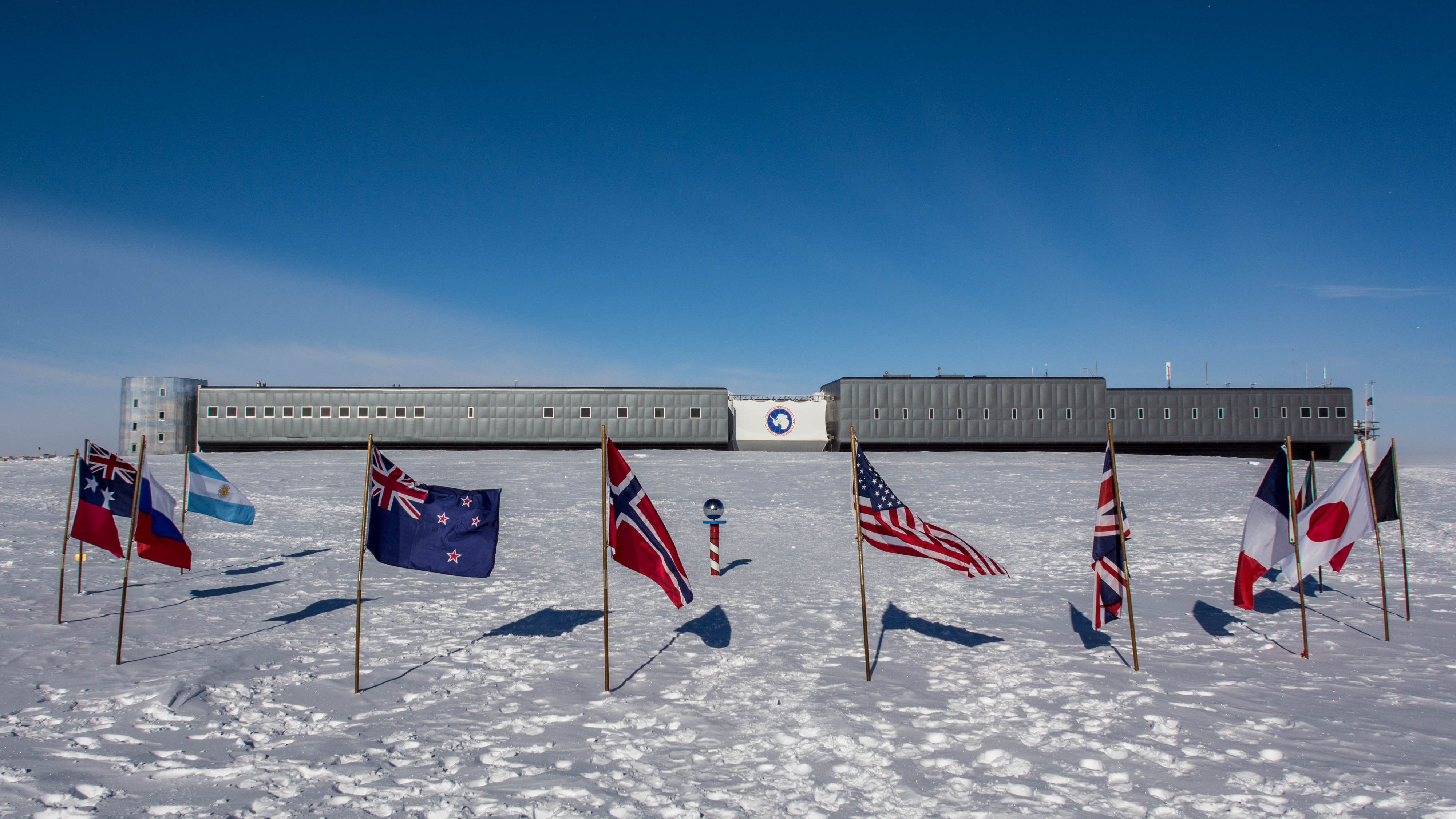 Flags surround a pole with a building in the background on a snowy landscape.