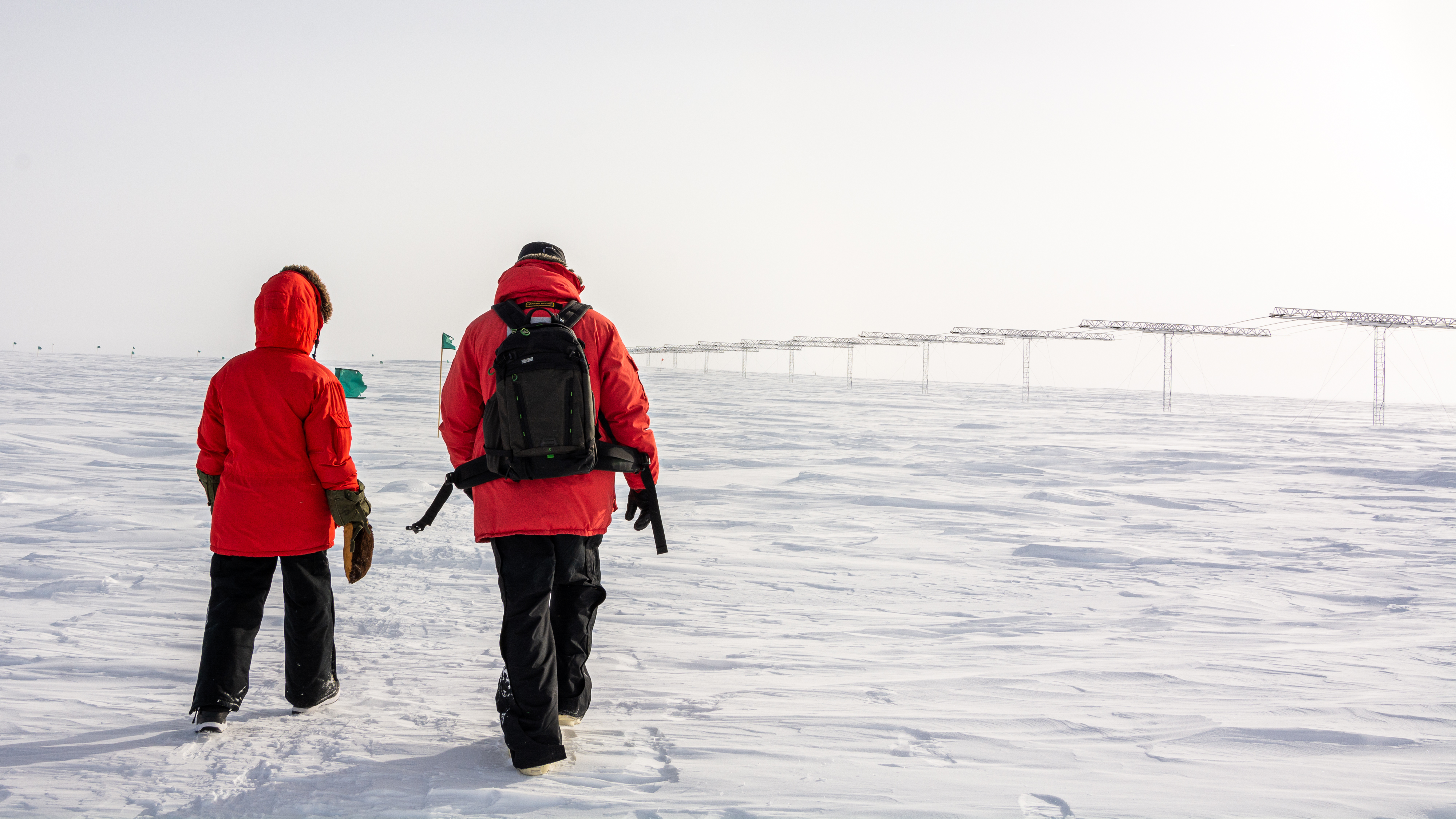 Two people in red coats walk towards a row of antennas.