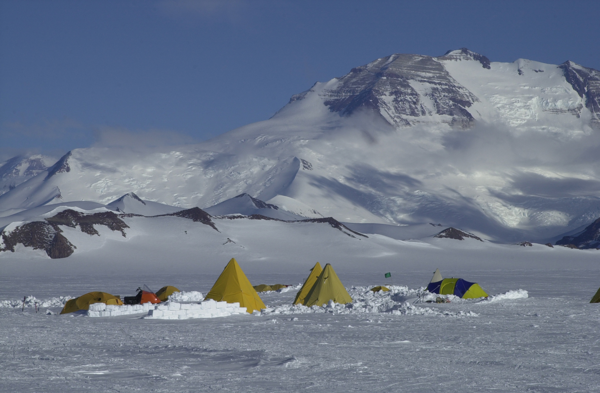 Yellow tents stand in front of mountains.