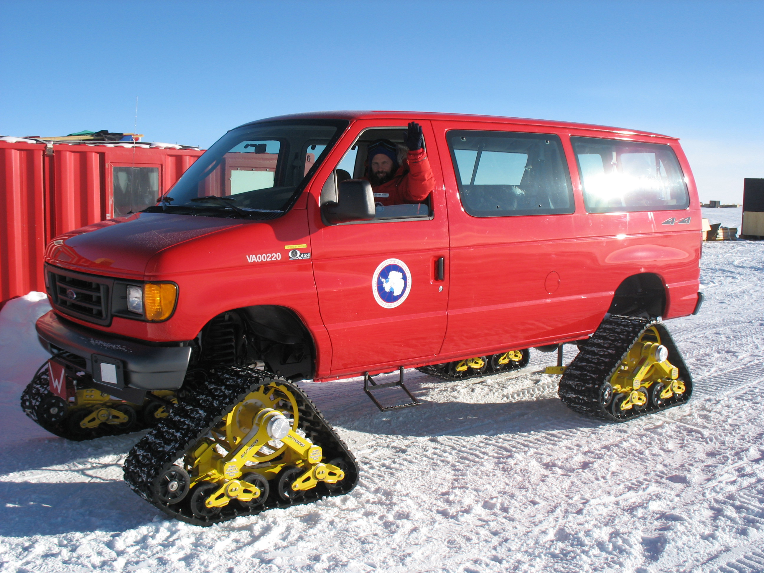 A red van with tractor treads on snow.