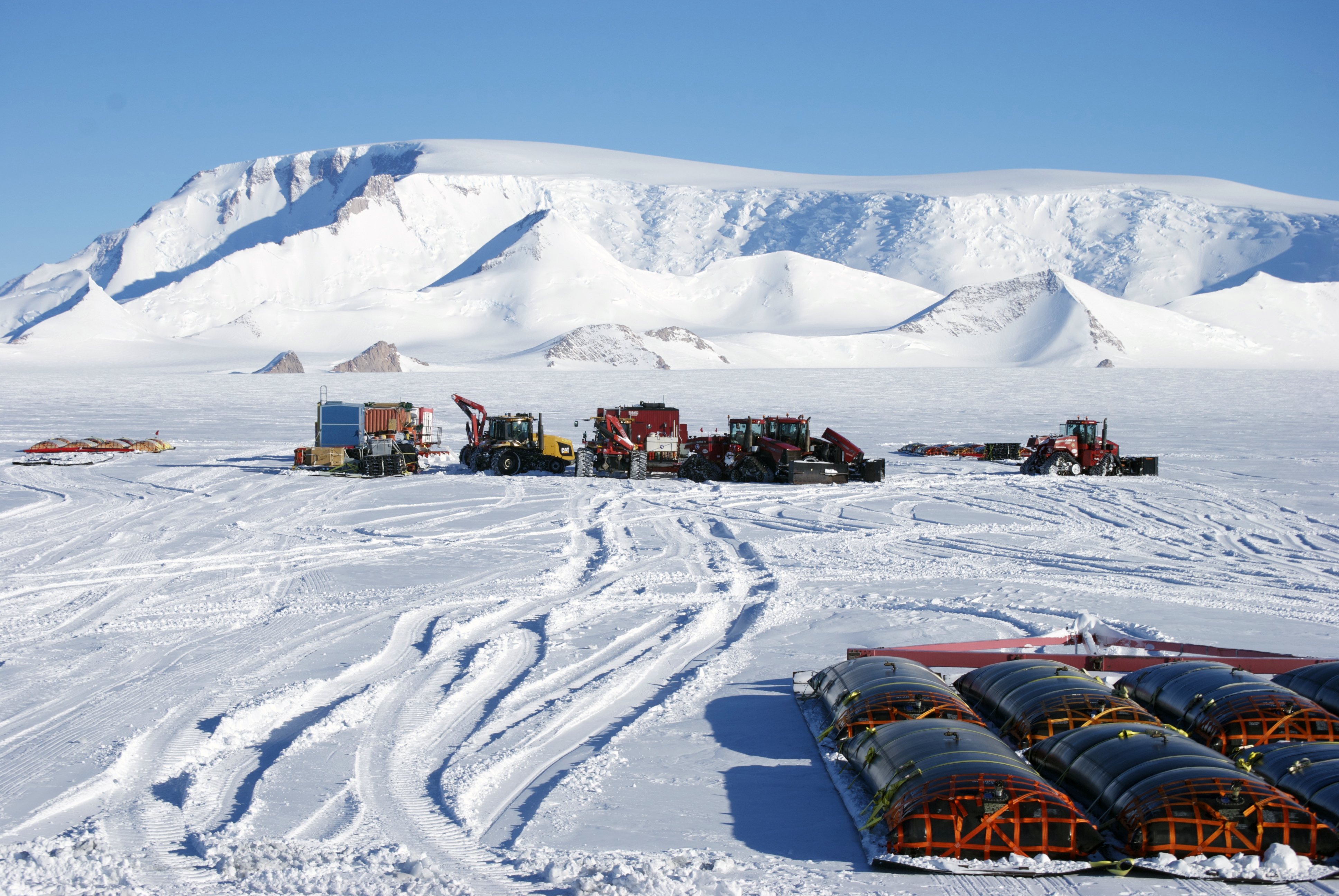 Tractors, sleds and fuel bladders on snow.