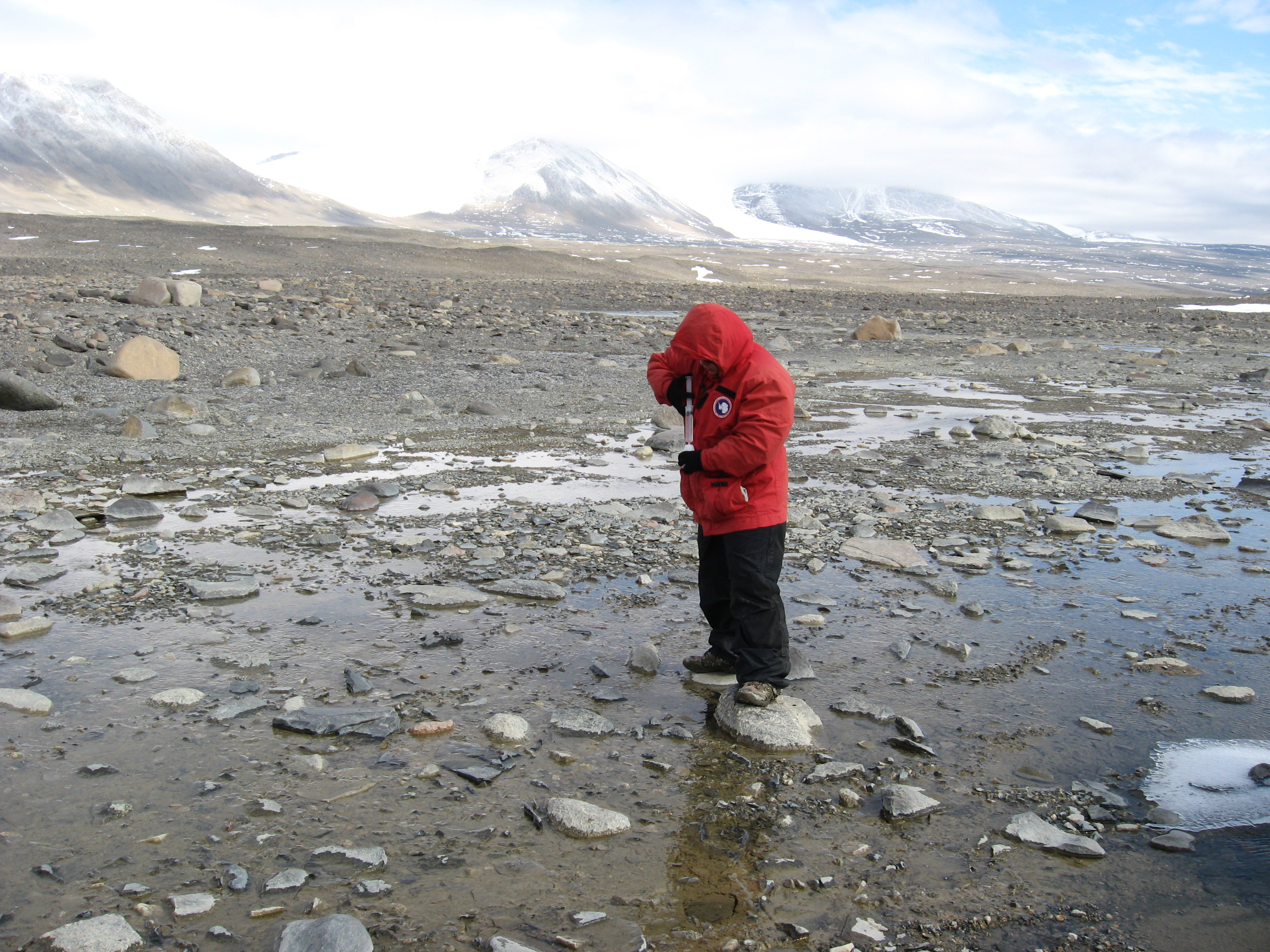 Person in red parka standing on rocky landscape.