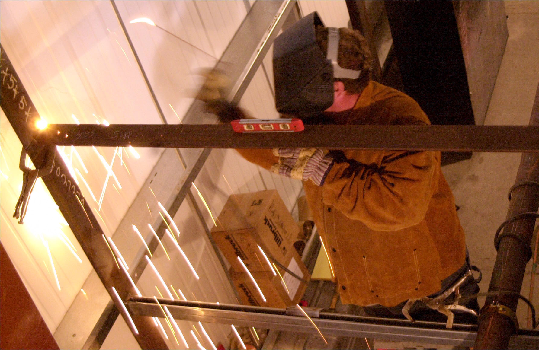 Sparks fly as a man welds pipes together indoors. 