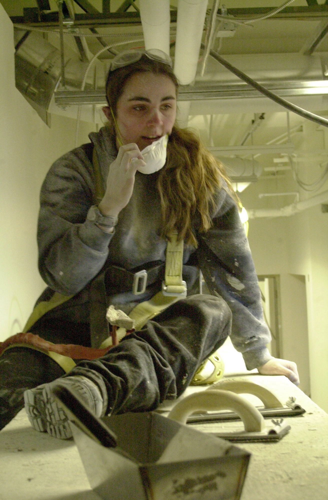 A women is covered in dust as she pulls off her dust mask. 