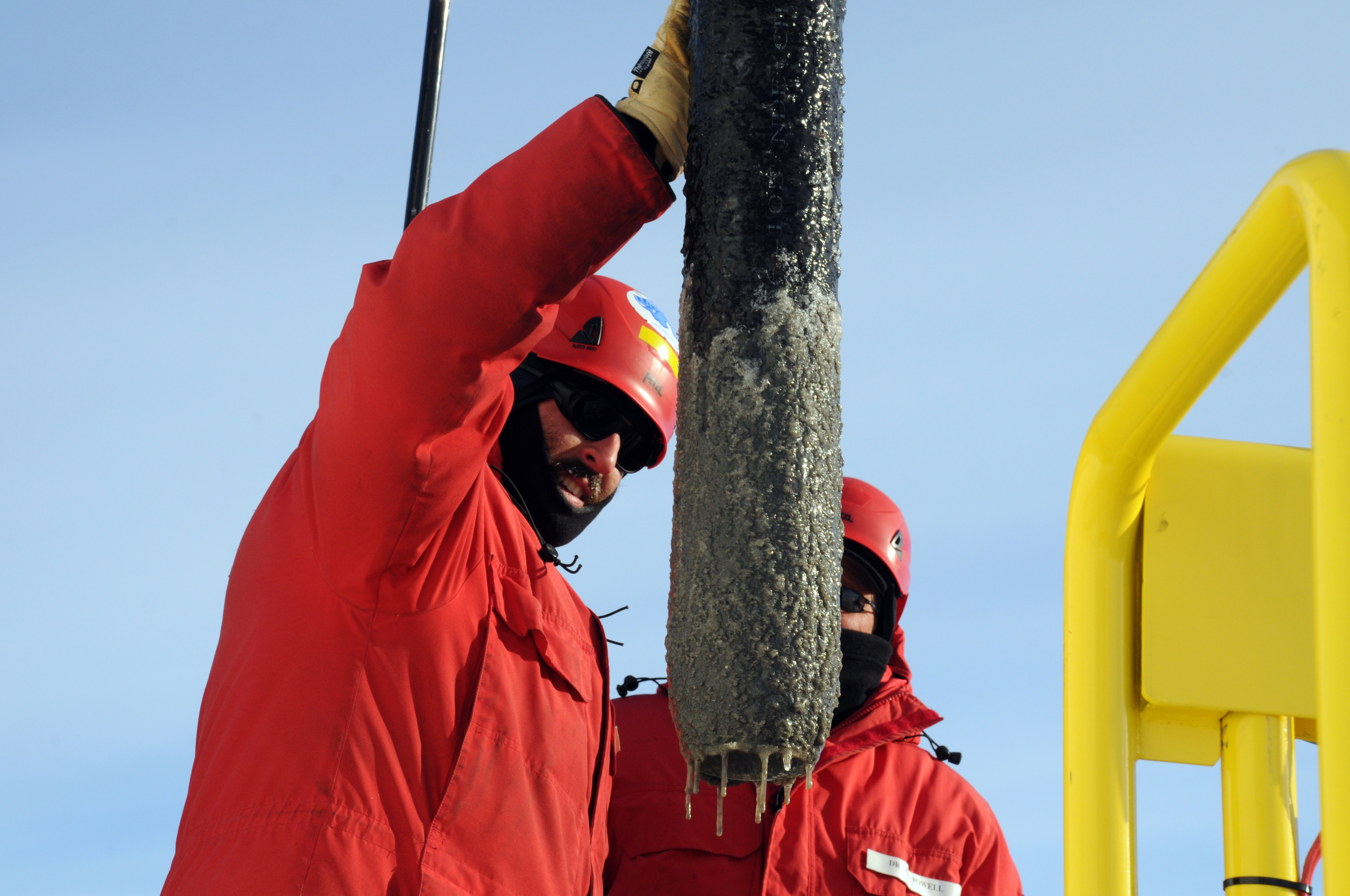 Two people handle muddy cylinder.