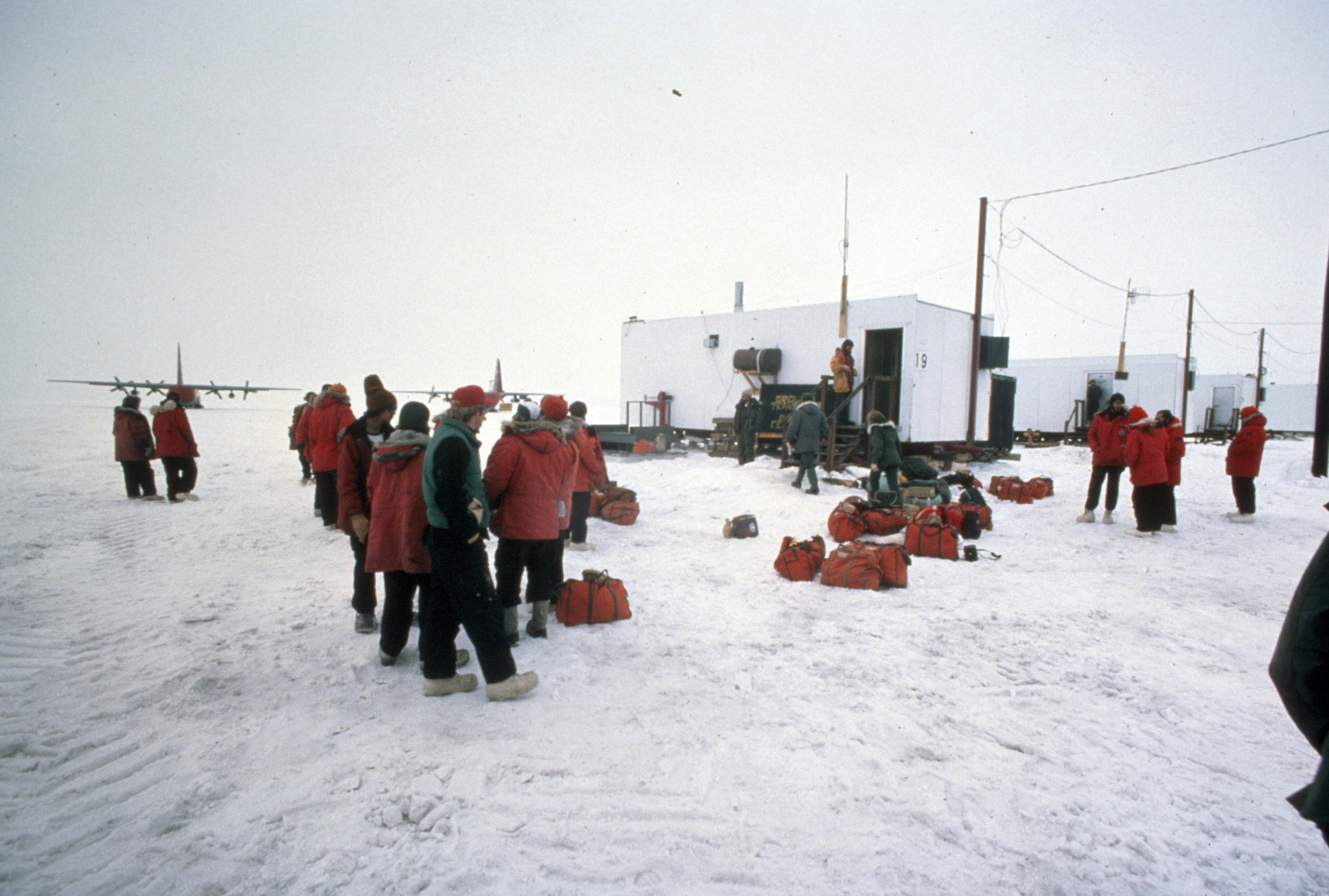 People dressed in heavy coats standing outside near small buildings.