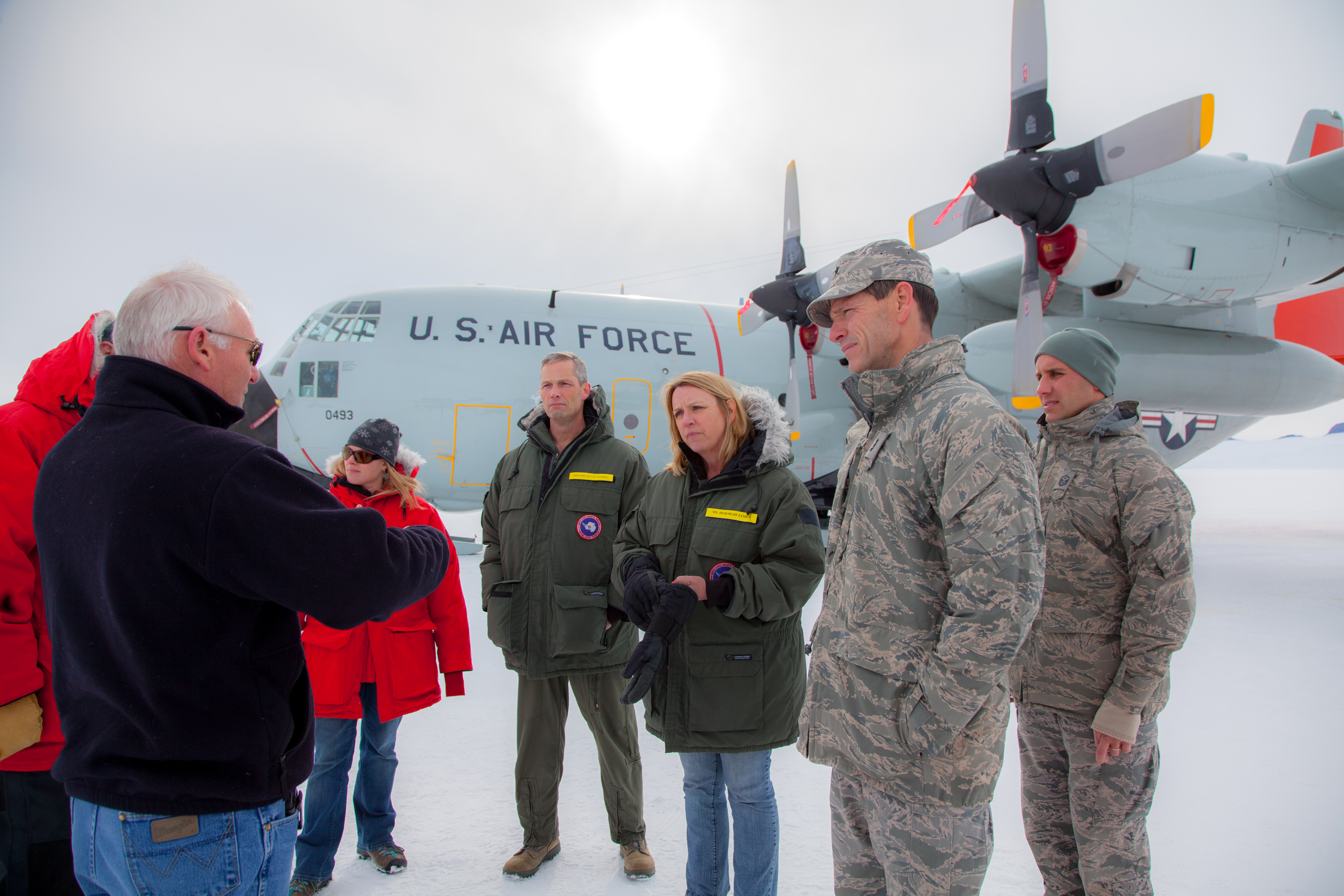 People talk in a group in front of an airplane.