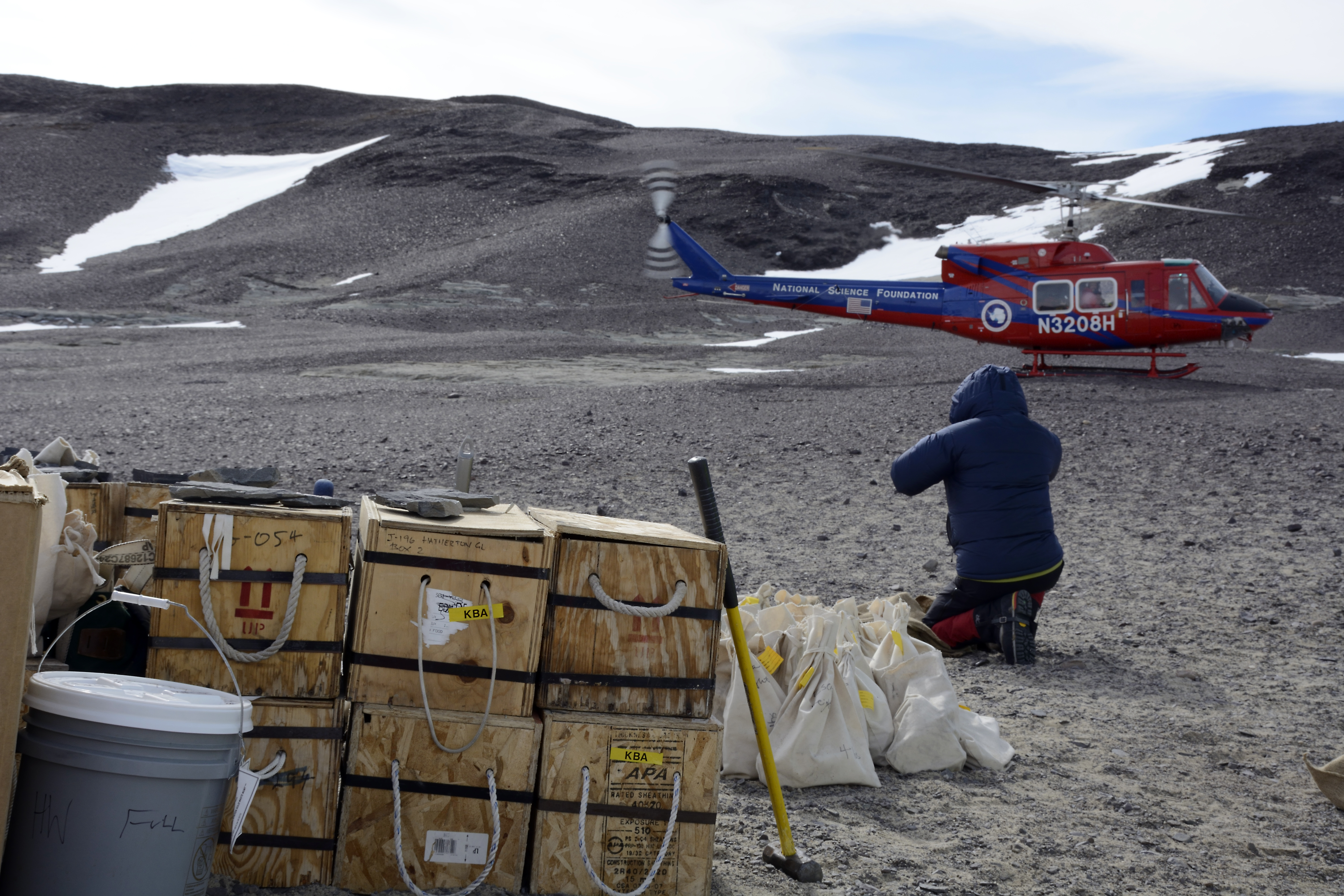 Person kneels down near boxes and bags and helicopter takes off.