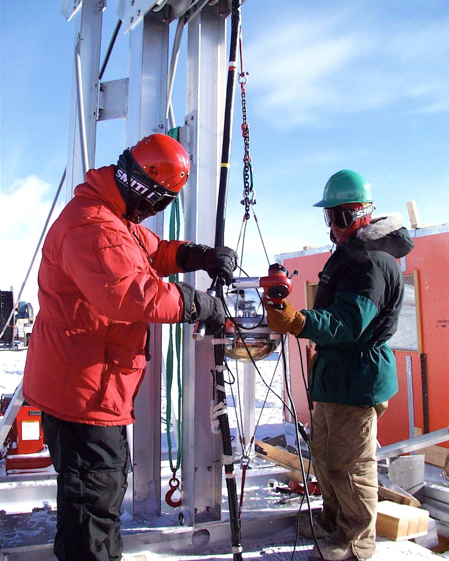 Two people work with a large ice-boring drill.