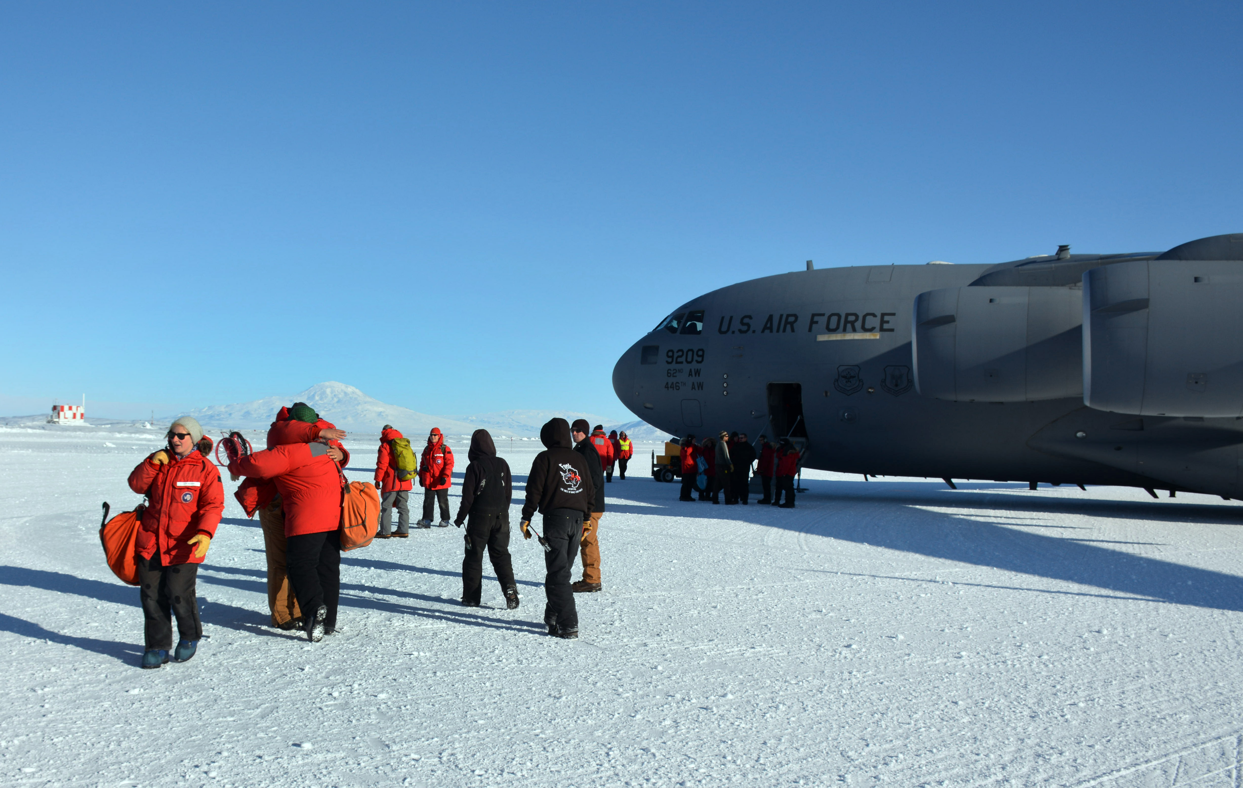 People carrying orange bags walk away from jet sitting on ice.